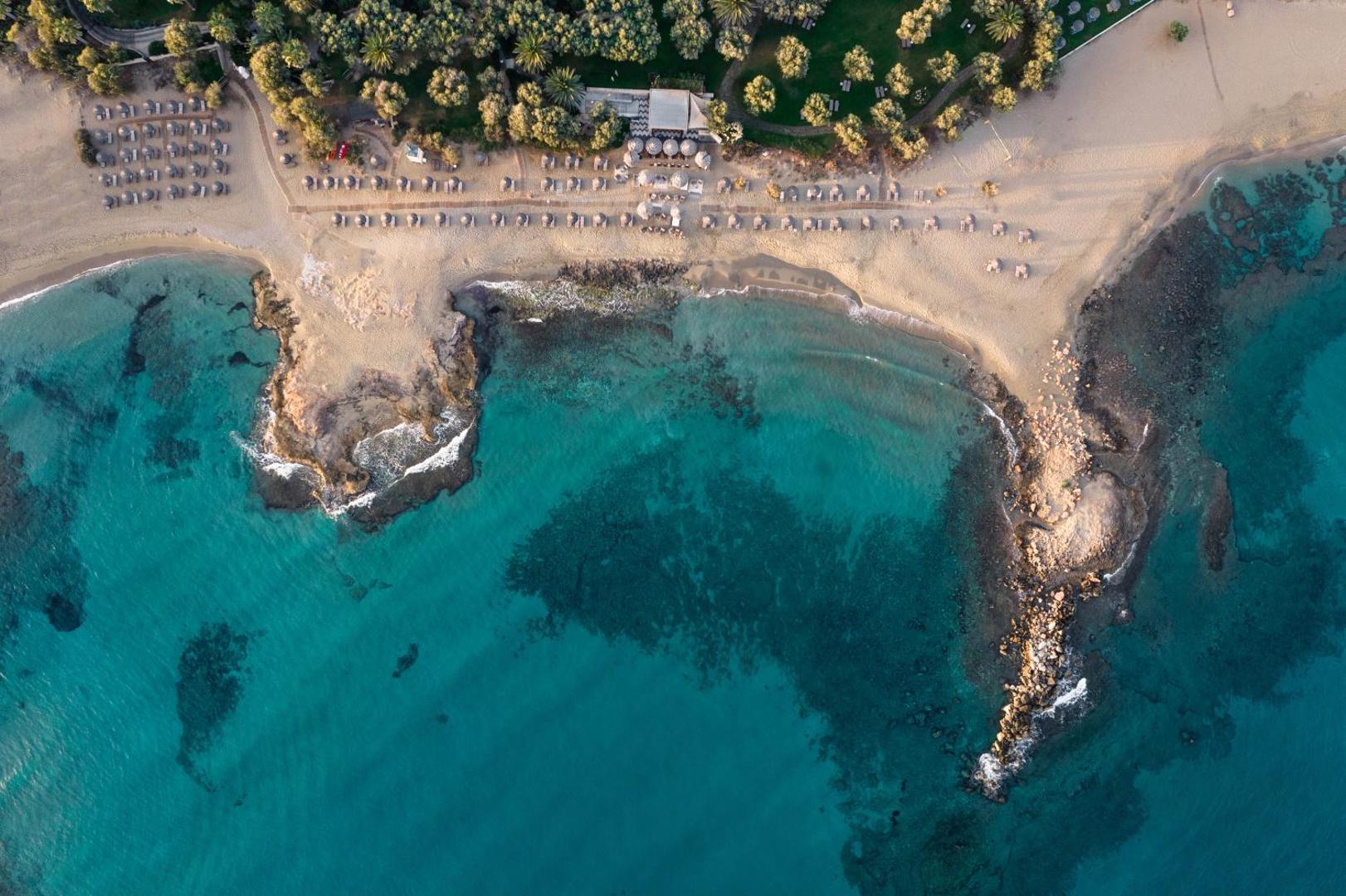 Phāea Cretan Malia Park viesnīcas aerofoto ar tirkīza krāsas līci, smilšu pludmali un zaļojošu dārzu Krētā