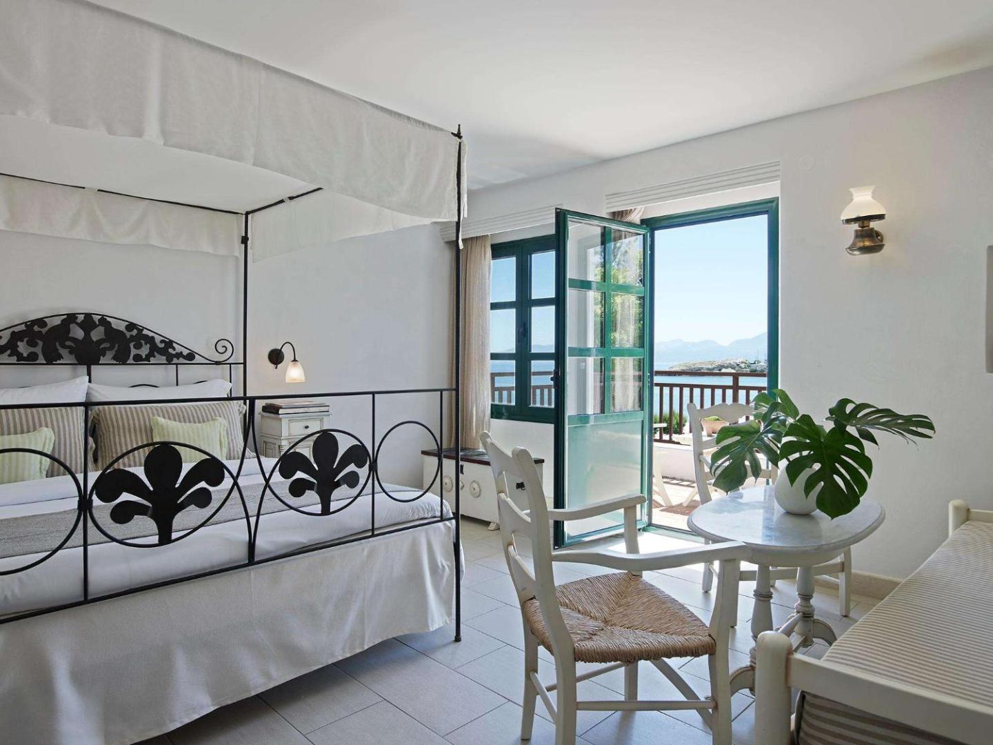 Creta Maris Resort gaišs numurs ar baldahīna gultu, antīka stila mēbelēm un atvērtām durvīm uz balkonu ar skatu uz jūru