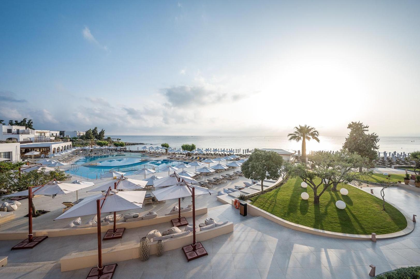 Creta Maris Resort plašā āra teritorija ar baseinu, saulessargiem un zālāju Hersonisā, Krētā, skats uz jūru saullēktā