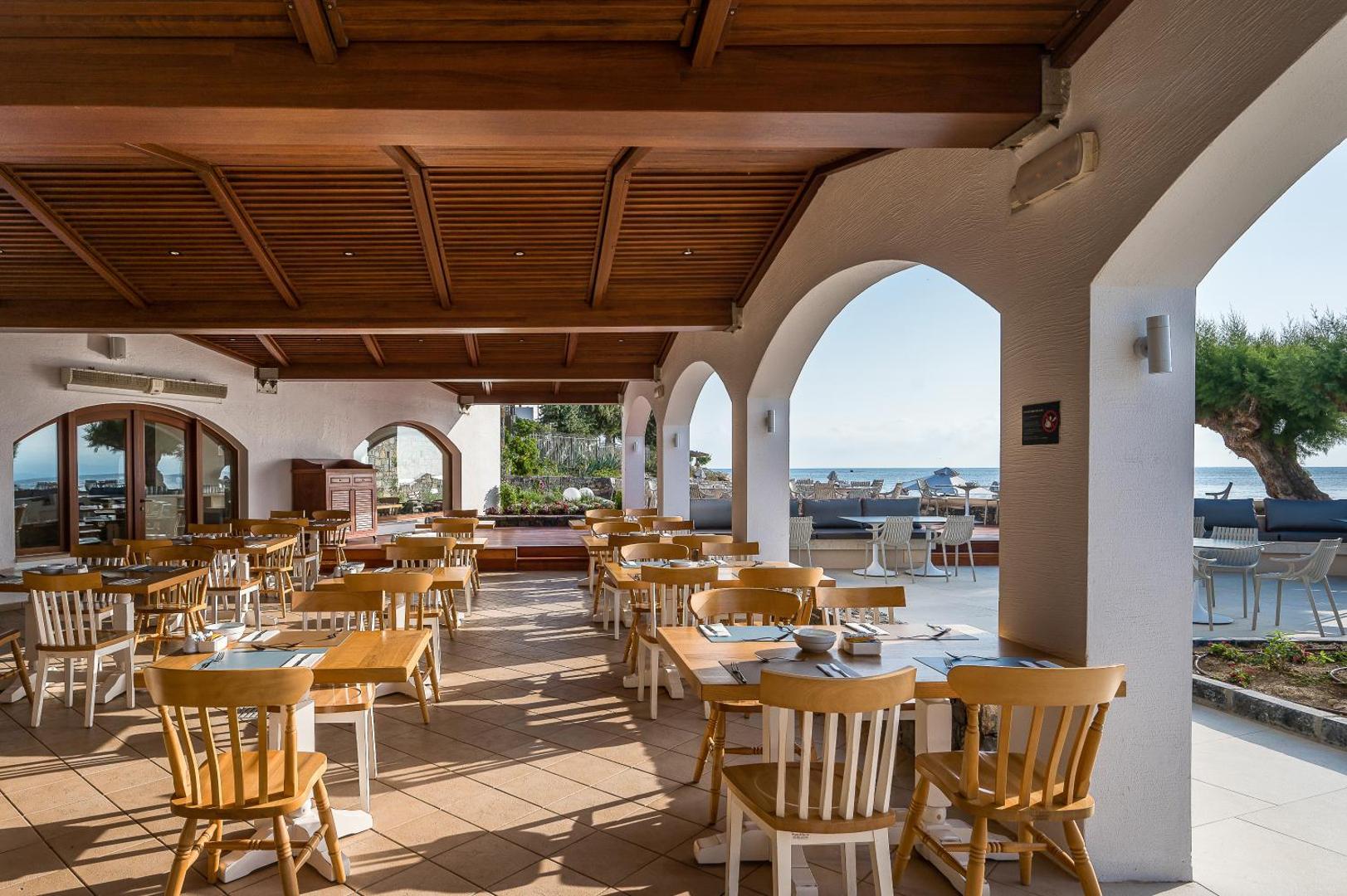 Creta Maris Resort restorāna āra terase ar koka mēbelēm un skatu uz jūru Hersonisā, Krētā — gaiša un mājīga atmosfēra