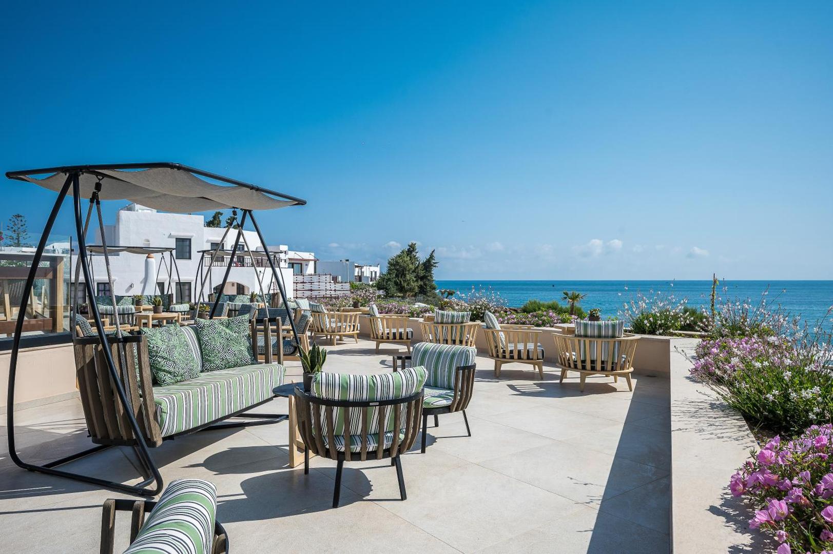 Creta Maris Resort āra terase ar stilīgiem šūpuļkrēsliem un skatu uz Vidusjūru saulainā dienā Krētas piekrastē