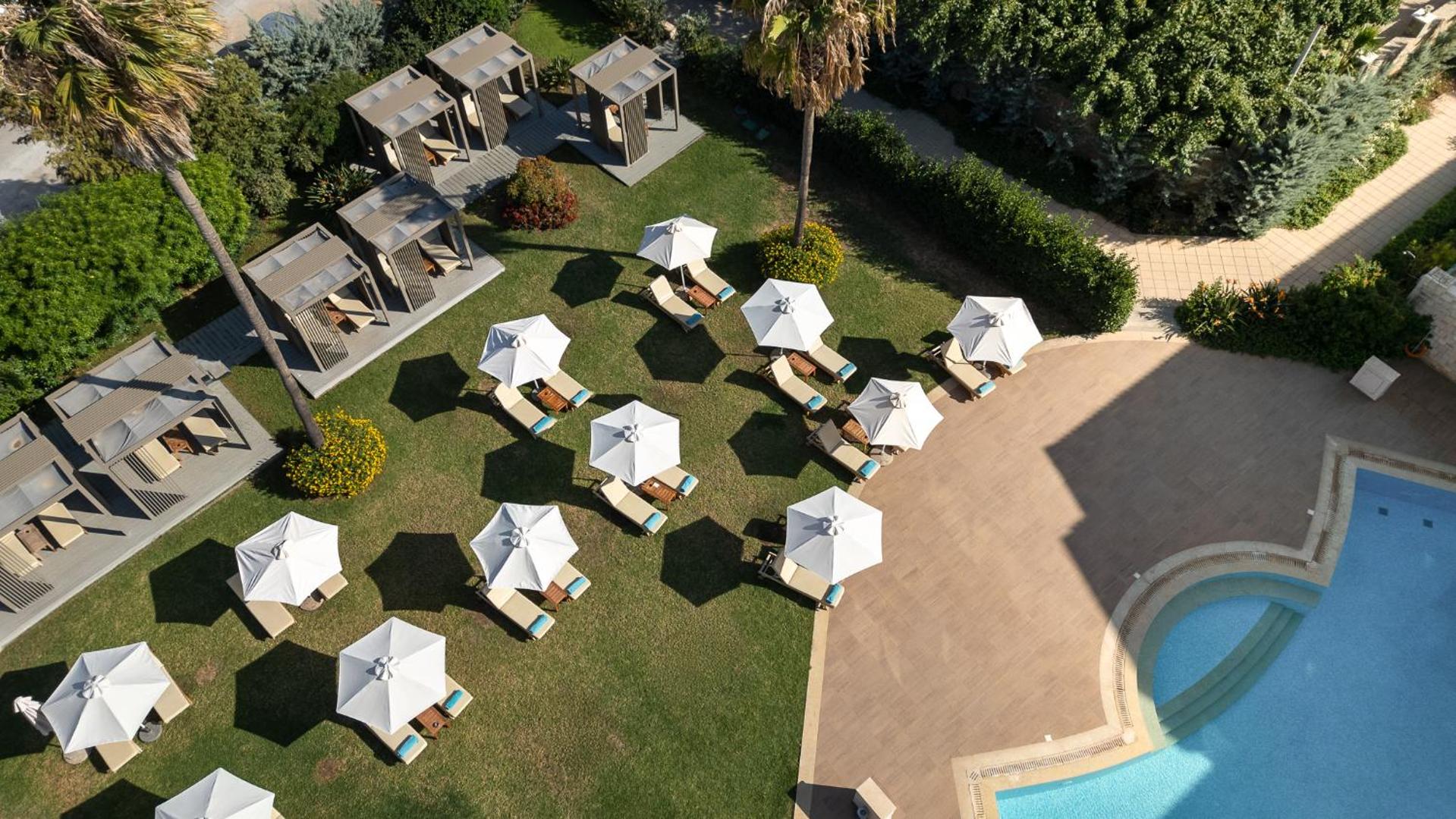 Aerofoto skats uz Castello Boutique Resort & Spa atpūtas zonu — balti saulessargi, zviļņi uz zaļa zālāja un baseina mala