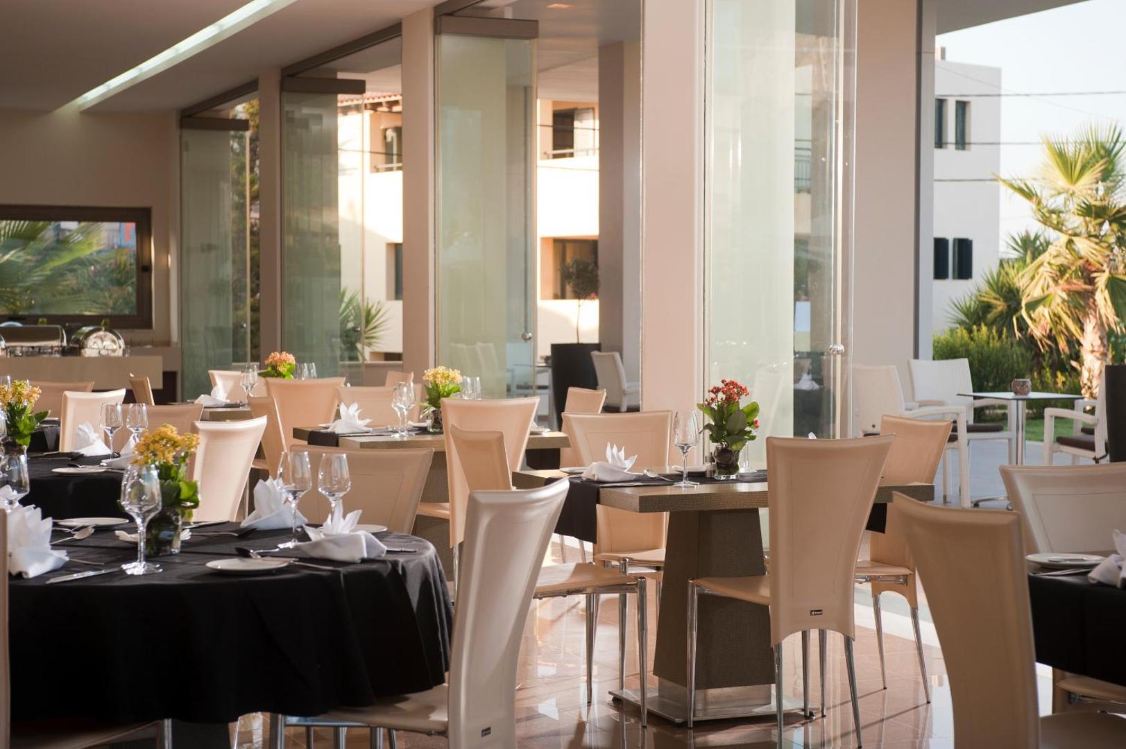 Elegants Castello Boutique Resort & Spa restorāns ar servētiem galdiem, melniem galdautiem un skatu uz dārzu caur lieliem logiem