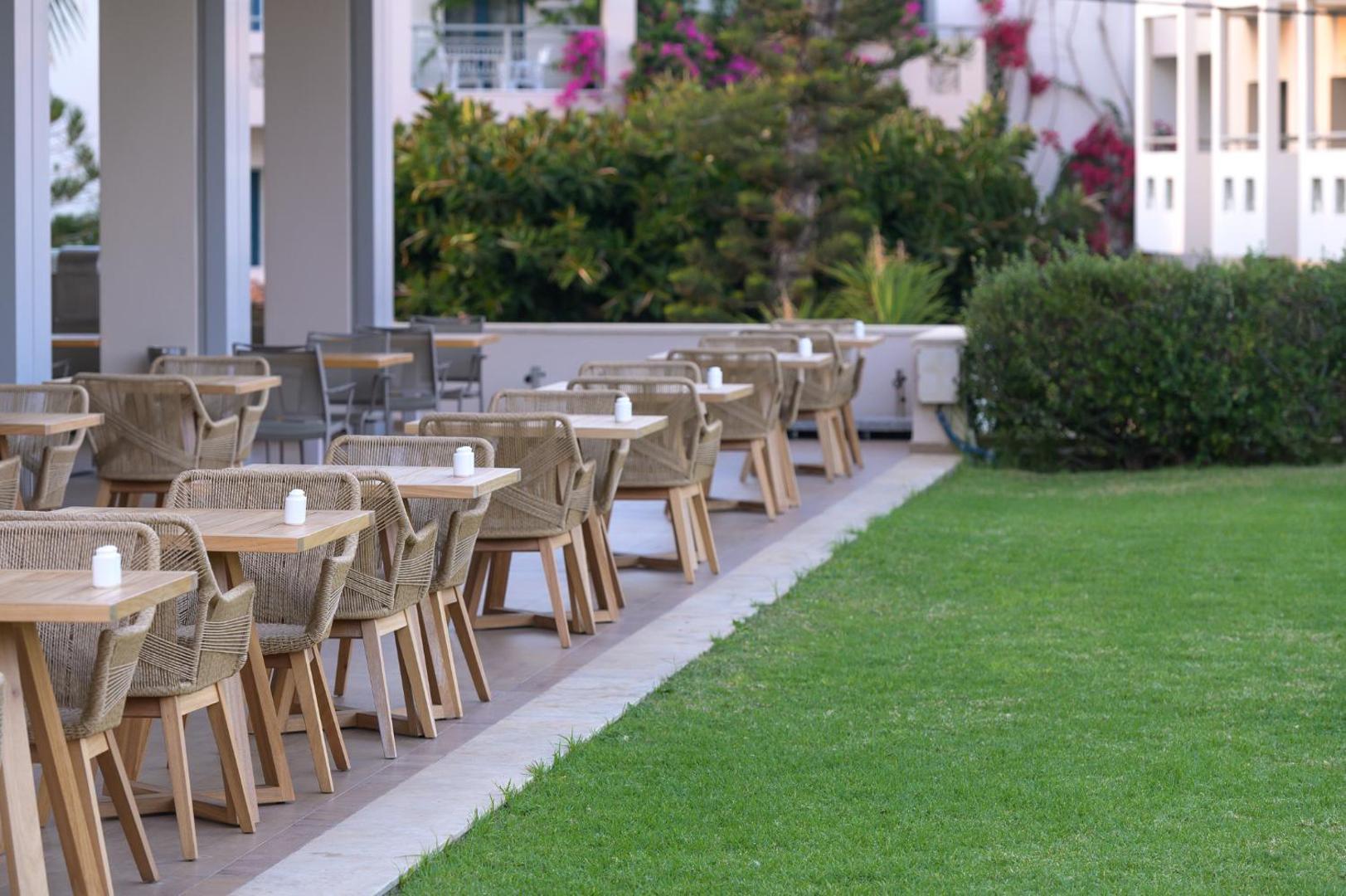 Castello Boutique Resort & Spa āra terases restorāns ar koka galdiem un pītiem krēsliem blakus koptam zaļam mauriņam Sisī ciemā, Krētā