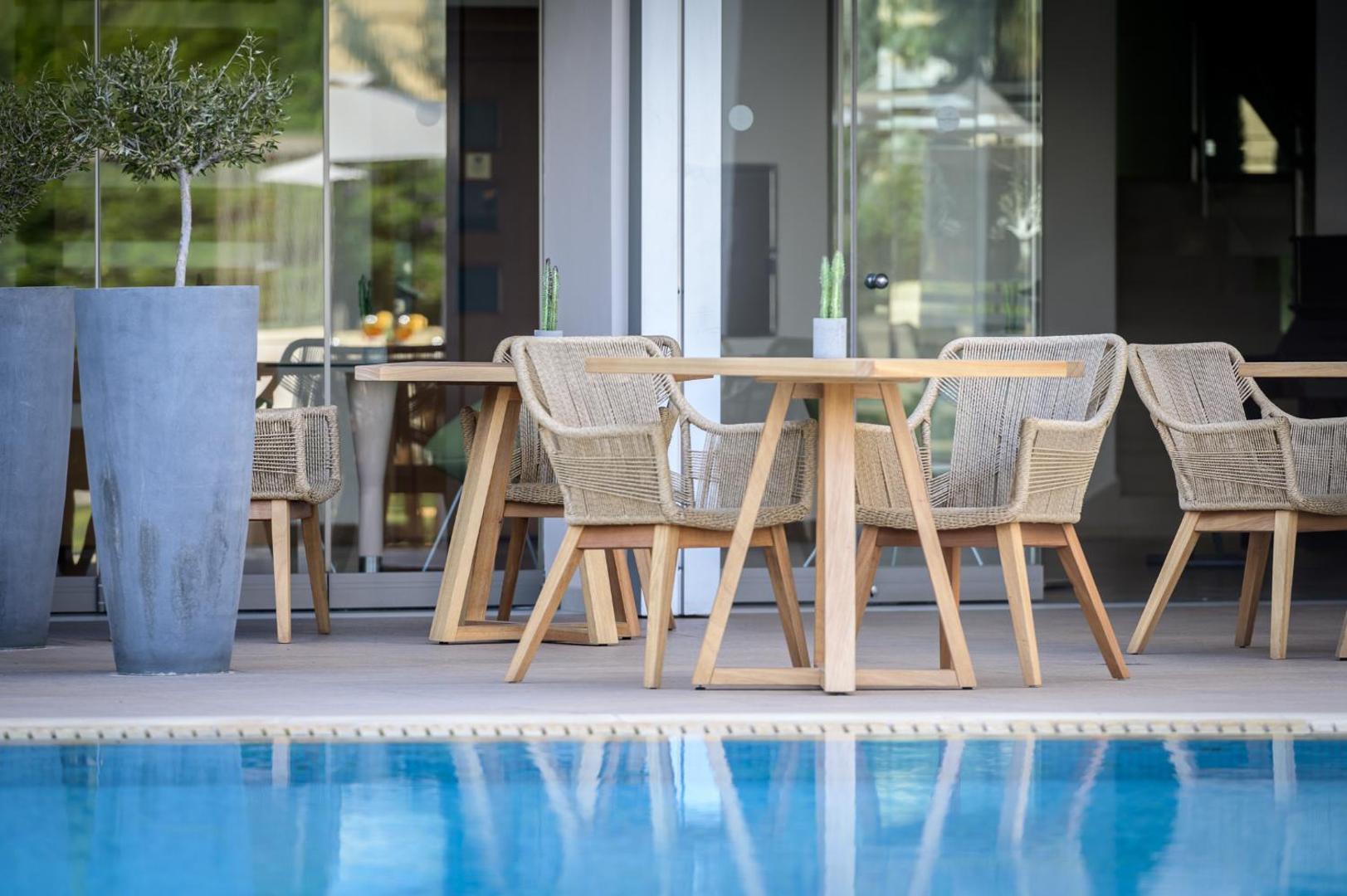 Castello Boutique Resort & Spa restorāna āra terase pie baseina — stilīgi pītie krēsli, koka galdi un dekoratīvi augi podos