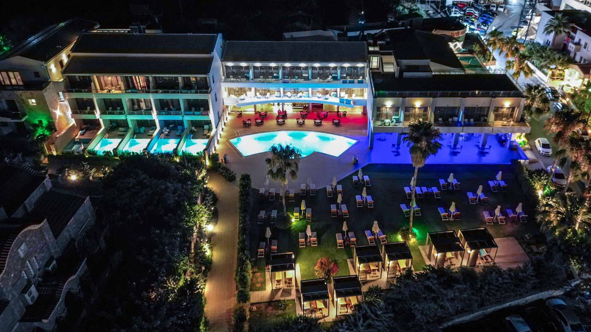 Castello Boutique Resort & Spa nakts skats no putna lidojuma uz izgaismotu baseinu, terasēm un dārzu ar atpūtas zonām Krētas piekrastē.