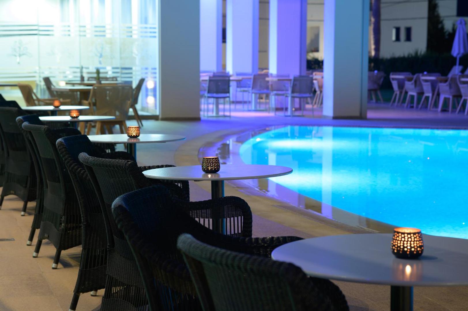 Vakara atmosfēra pie Castello Boutique Resort & Spa baseina ar galdiņiem, svecēm un zilu apgaismojumu āra terasē
