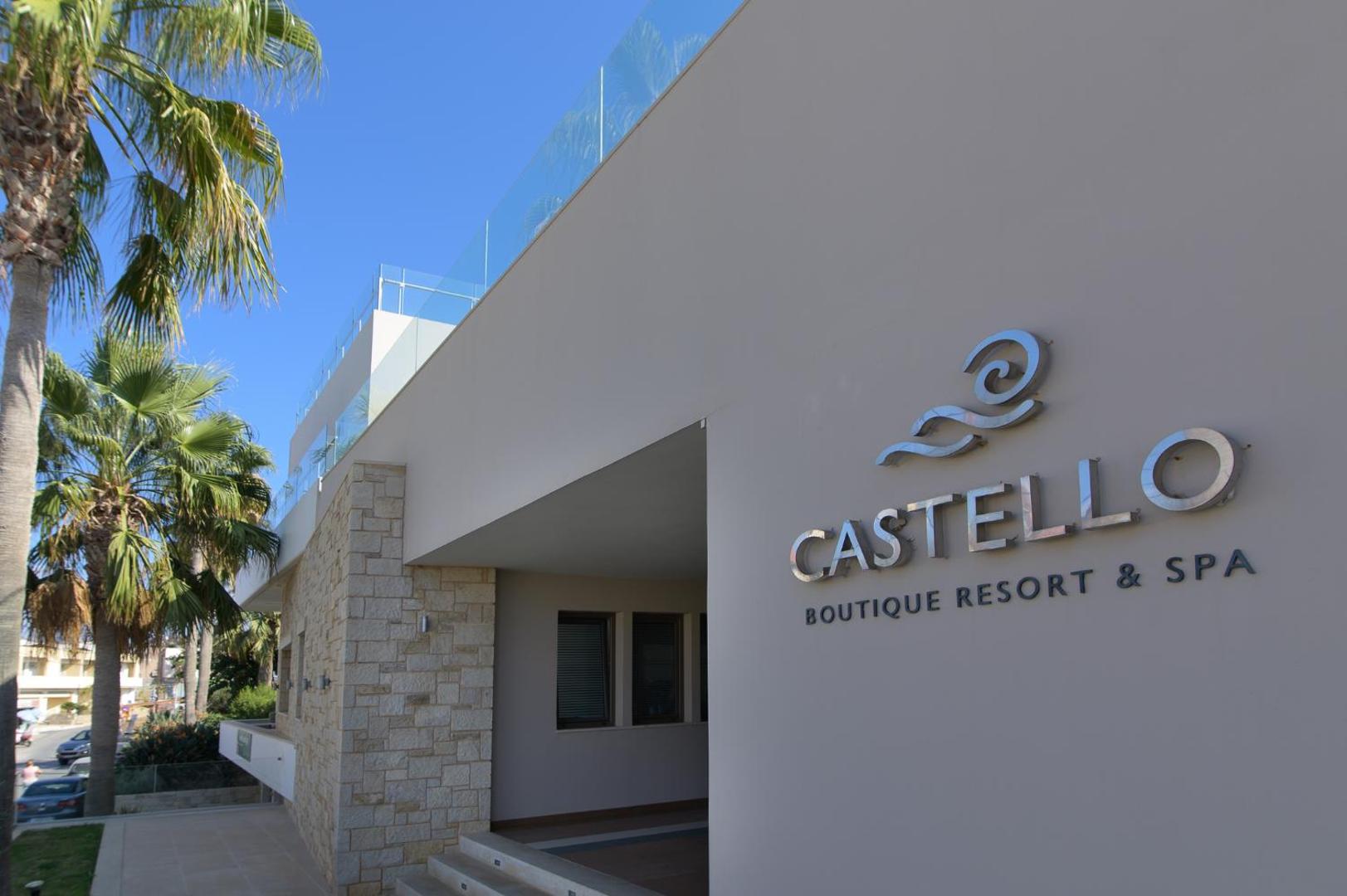 Castello Boutique Resort & Spa ieeja ar viesnīcas logo uz modernas ēkas fasādes, fonā redzamas palmas un zilas debesis.