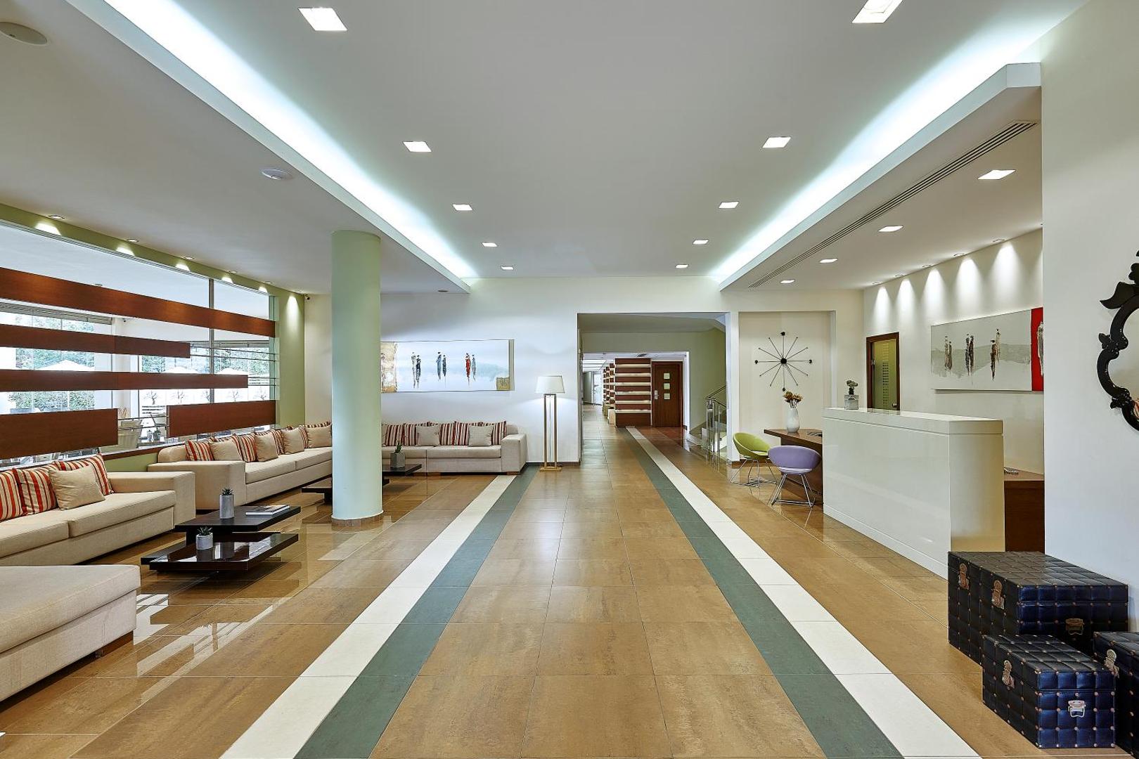 Castello Boutique Resort & Spa modernais vestibils ar gaišu interjeru, ērtiem dīvāniem, recepcijas leti un stilīgiem dizaina elementiem Krētā