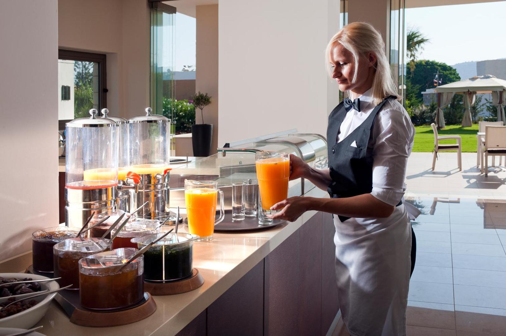 Viesnīcas darbiniece gatavo svaigi spiestu apelsīnu sulu Castello Boutique Resort & Spa brokastu bufetē Krētas kūrortā