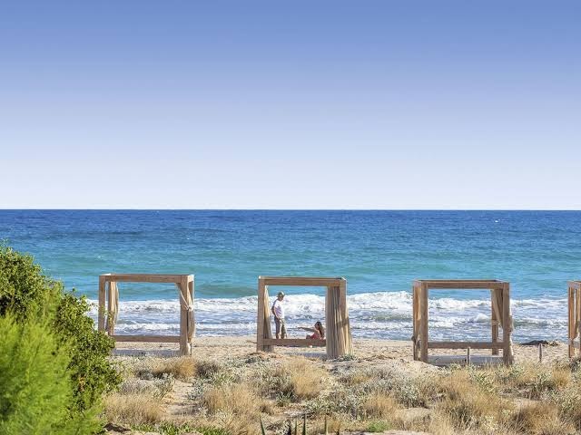 Bella Beach Hotel privātā pludmale ar koka atpūtas nojumēm un skatu uz zilo jūru Krētas piekrastē saulainā dienā