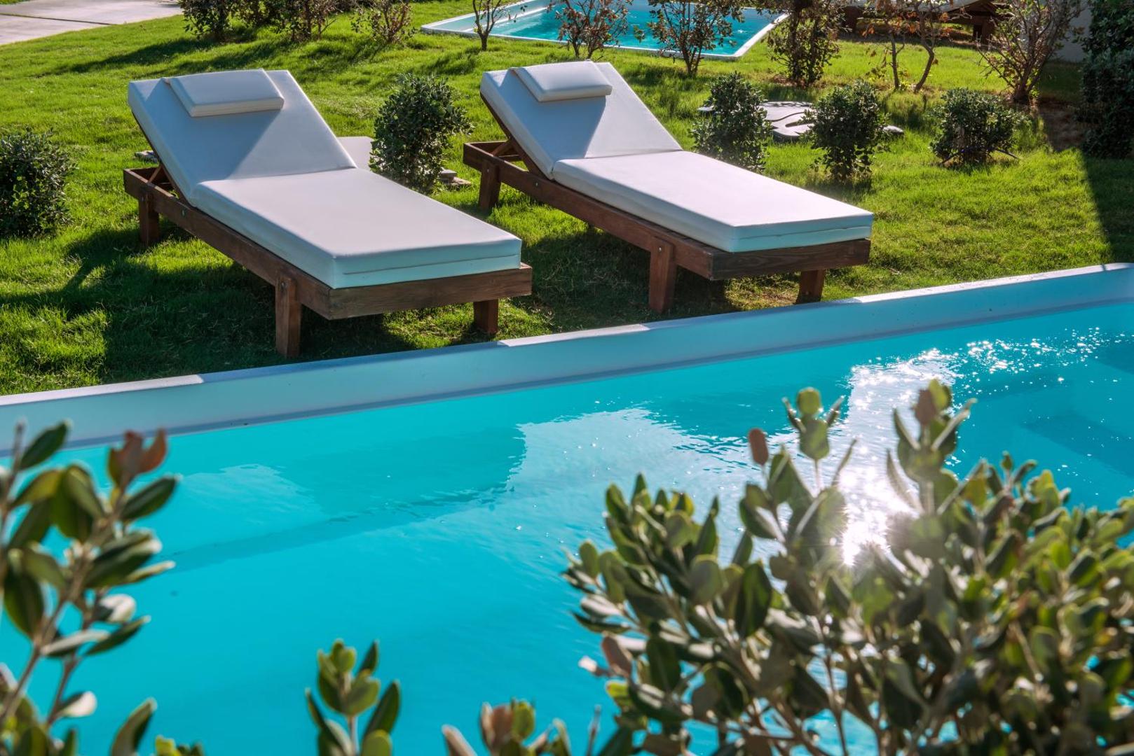 Tuvplāns ar sauļošanās krēsliem pie dzidra baseina Bella Beach Hotel dārzā, Stalidas reģionā