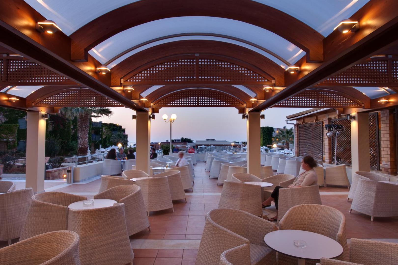 Bella Beach Hotel segtā āra terase ar pītiem krēsliem un romantisku apgaismojumu vakara stundās