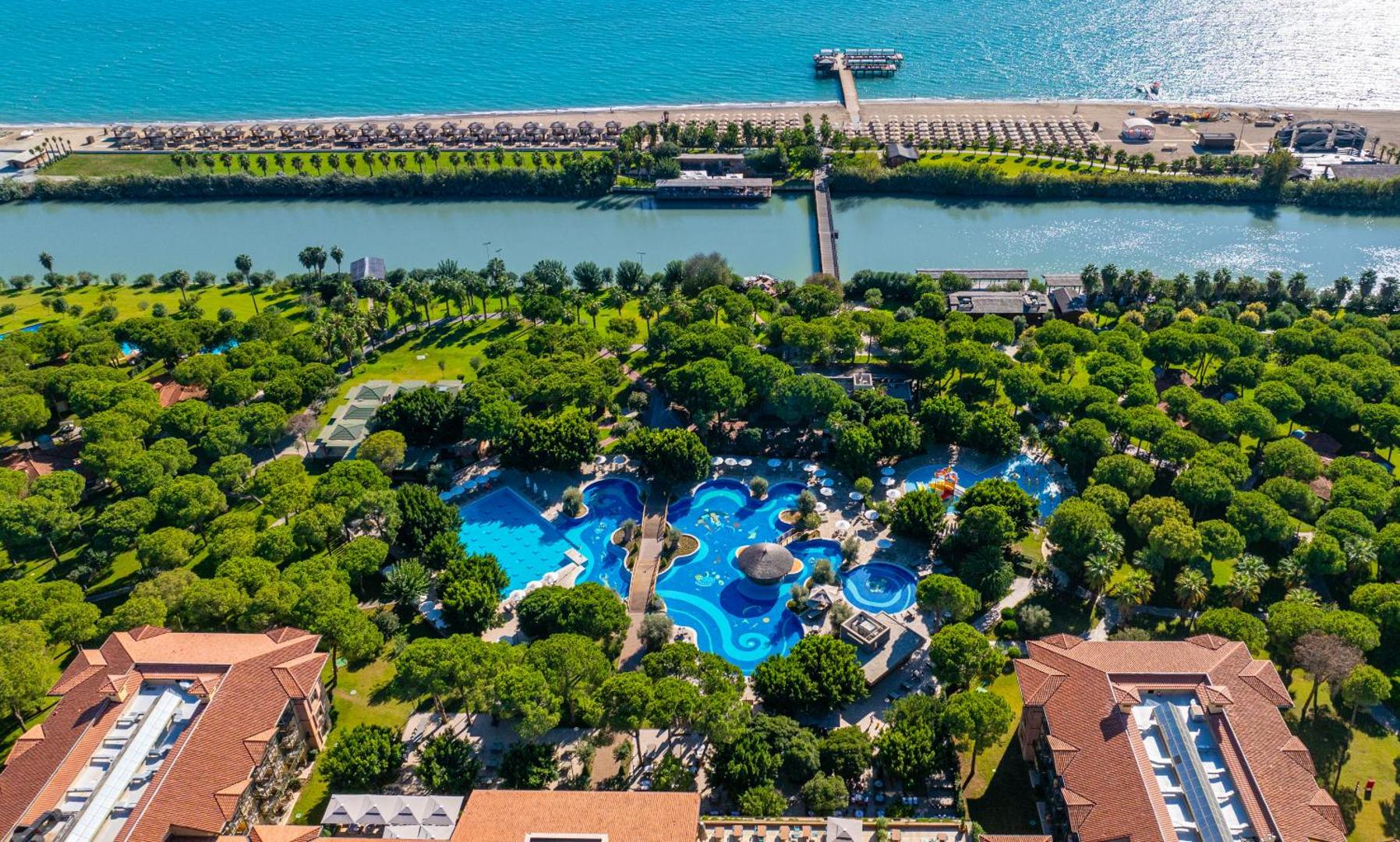 Gloria Golf Resort aerofotoattēls Belekā — plaša zaļā teritorija ar baseiniem, upi un privāto pludmali Vidusjūras piekrastē