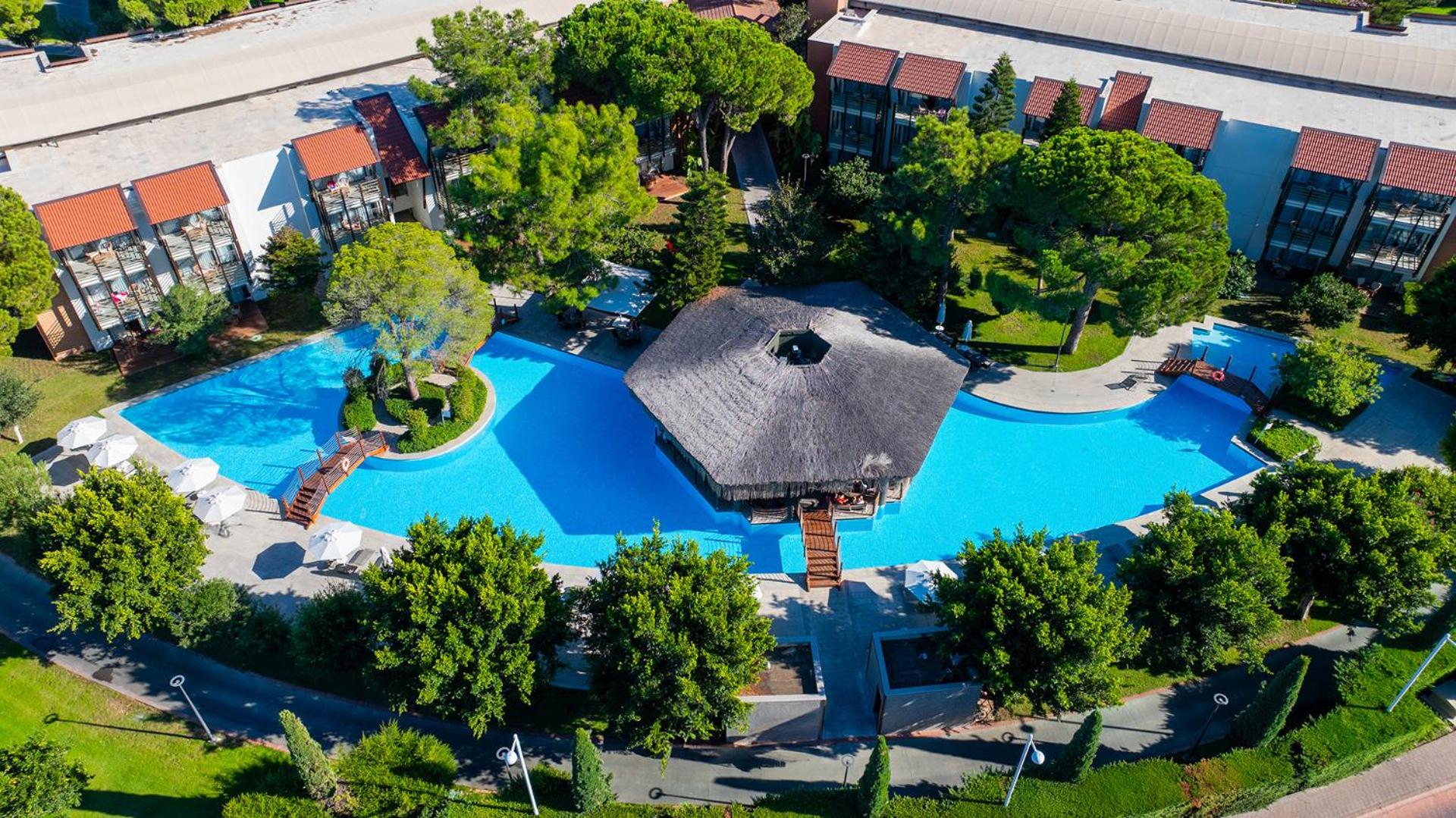 Gloria Golf Resort kopskats no augšas uz baseinu ar bāru centrā, dārzu un viesnīcas ēkām Belekā