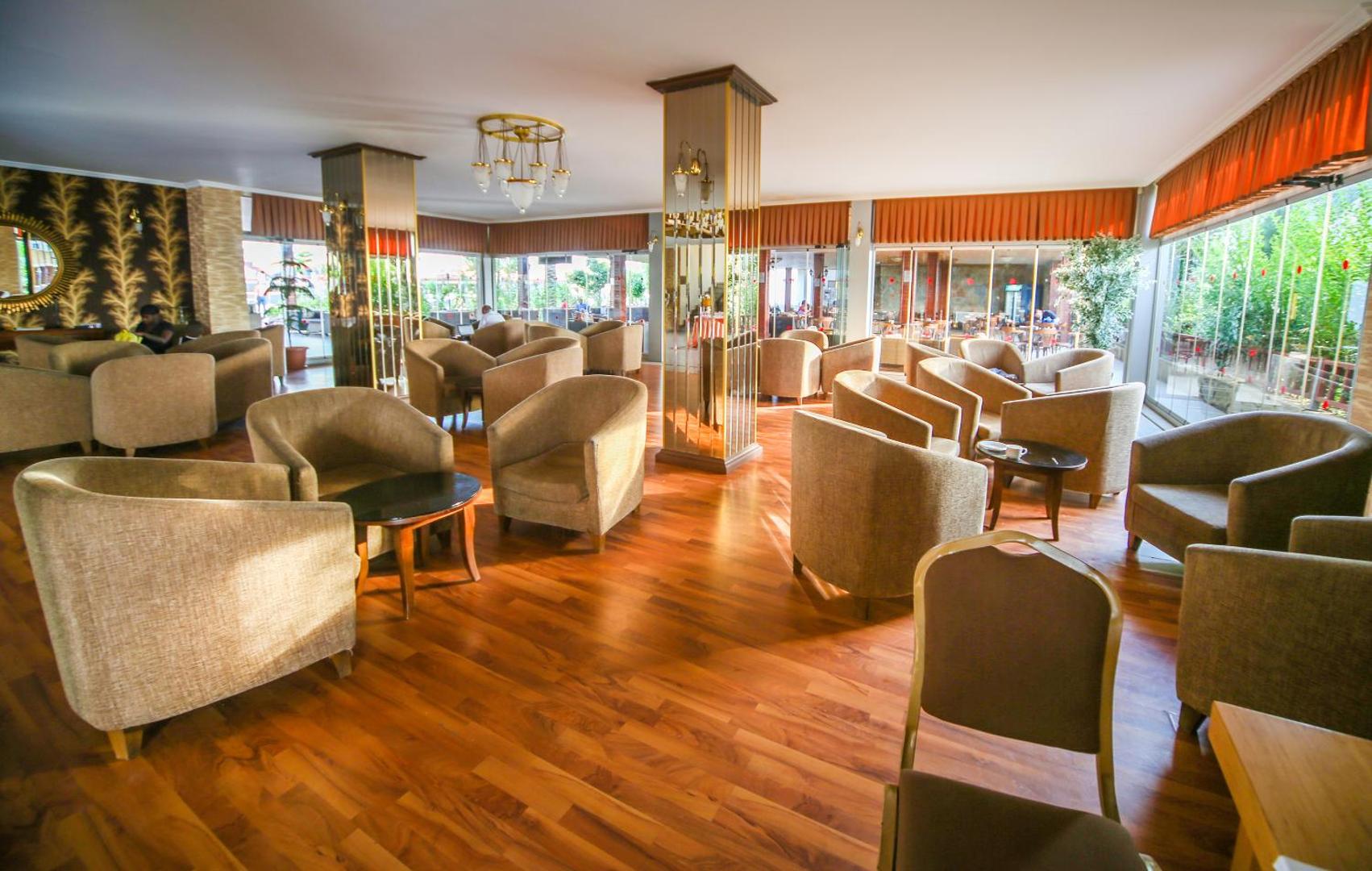 Eftalia Village lobby bārs ar ērtiem atpūtas krēsliem, koka grīdu un plašiem logiem, kas vērsti uz dārzu.