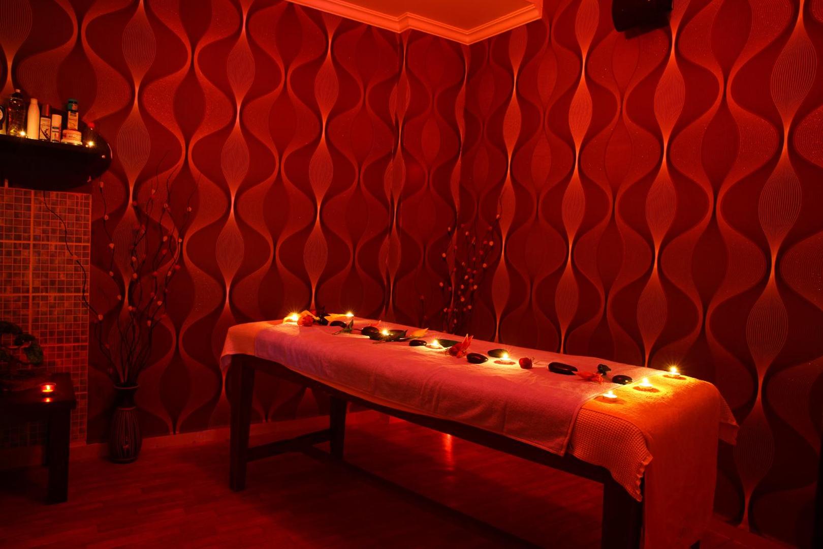 Eftalia Village spa procedūru telpa ar masāžas galdu, svecēm un siltu, sarkanu apgaismojumu romantiskai noskaņai.