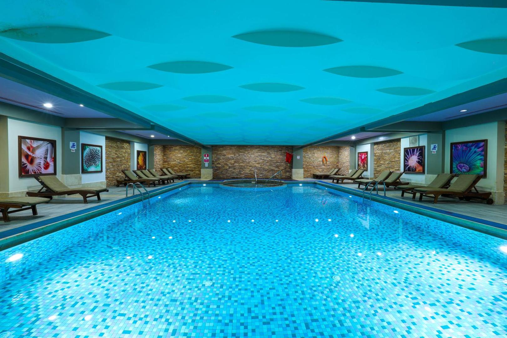 Crystal Palace Luxury Resort & Spa iekštelpu baseins ar zilu apgaismojumu, guļamkrēsliem un akmens sienu apdari spa centrā
