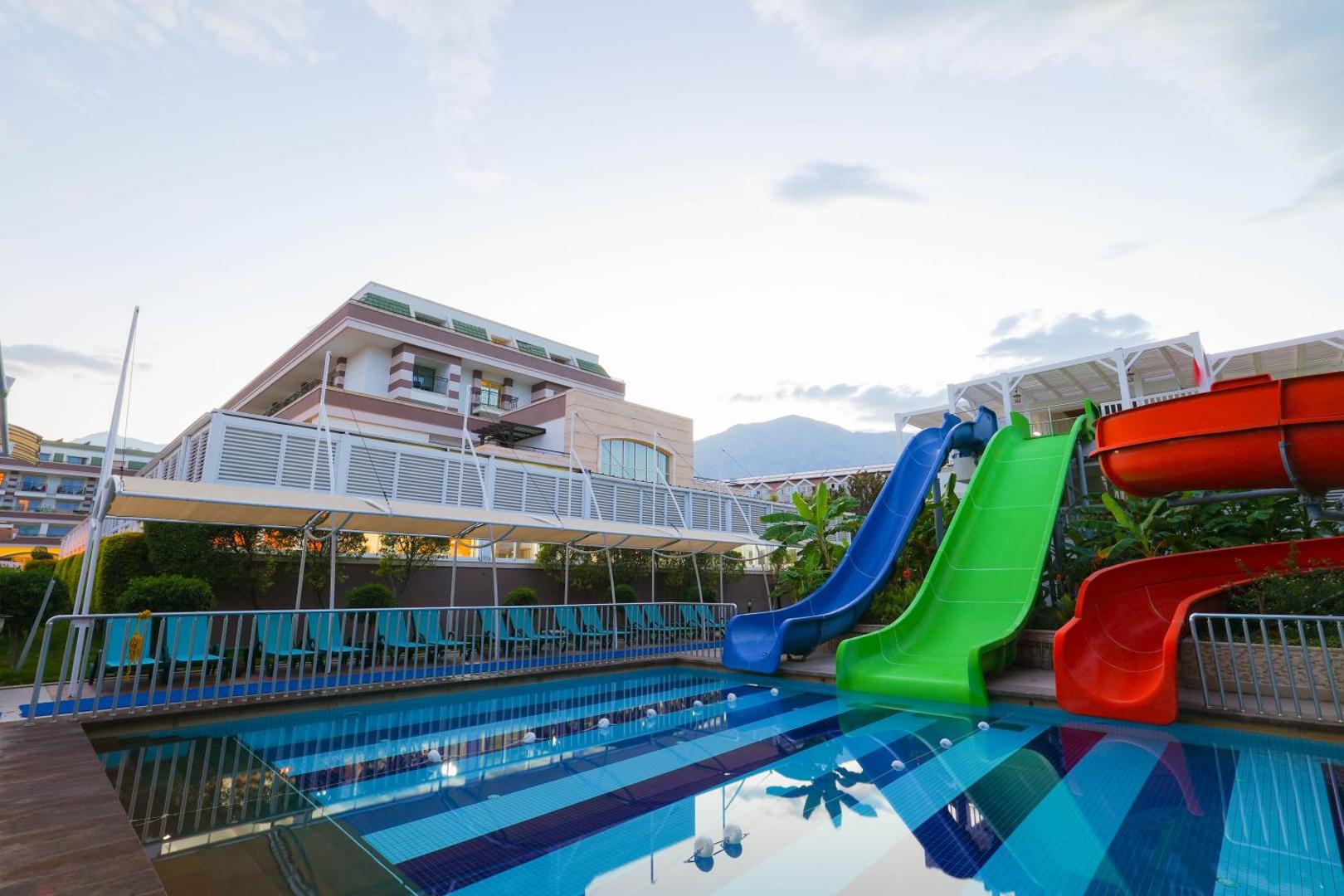 Crystal Palace Luxury Resort & Spa āra baseins ar krāsainiem ūdens slidkalniņiem un skatu uz kalniem Sides reģionā, Turcijā.