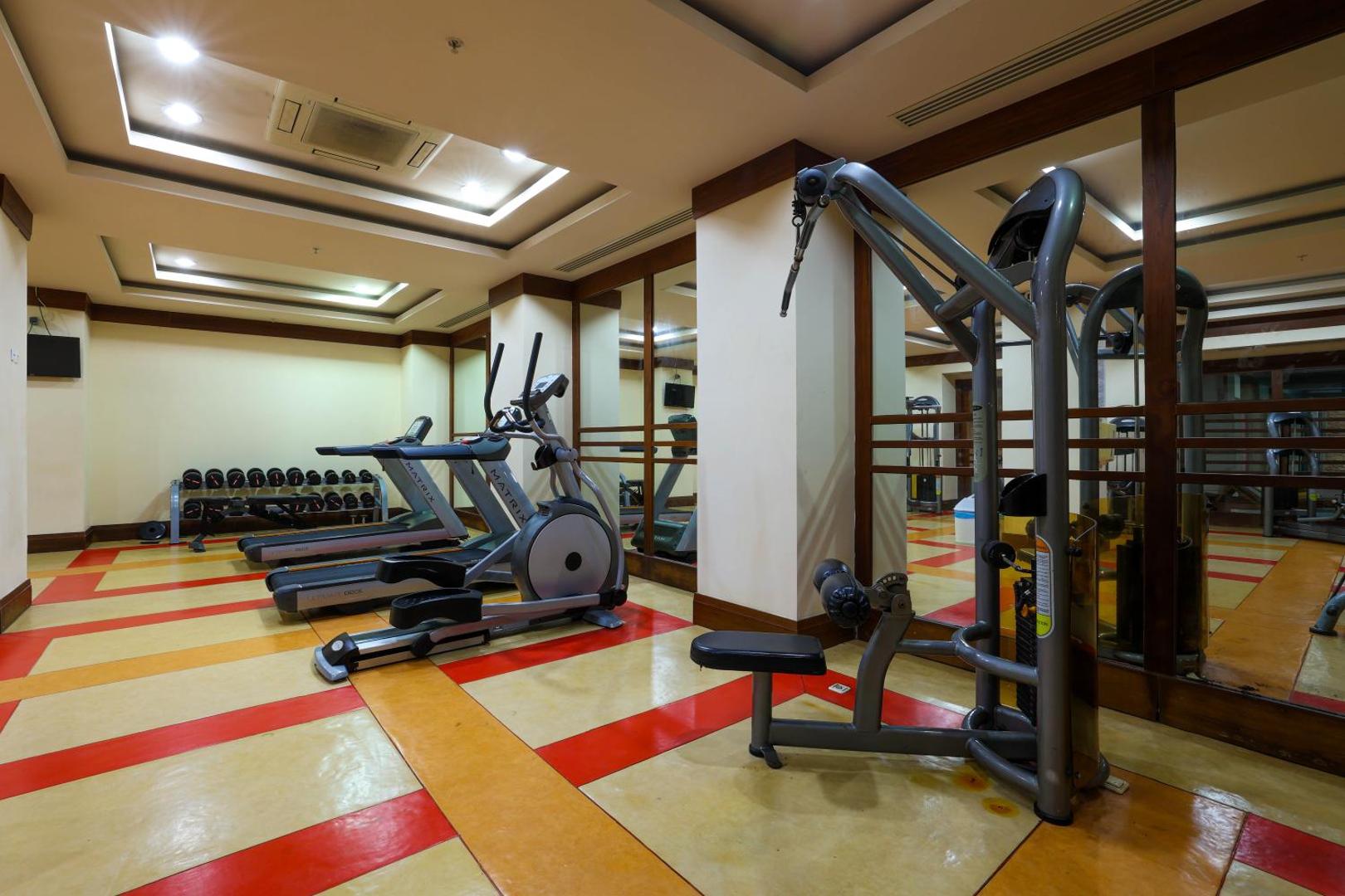 Crystal Palace Luxury Resort & Spa fitnesa centrs ar Matrix skrejceliņiem un spēka trenažieriem — gaiša telpa ar spoguļiem un hanteļu zonu
