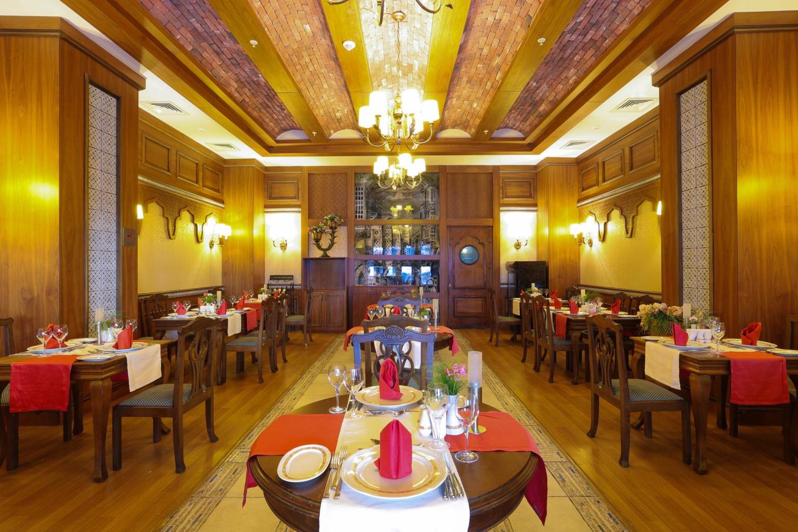 Crystal Palace Luxury Resort & Spa klasiska stila restorāns ar koka apdari, greznām lustrām un svinīgi klātiem galdiem.