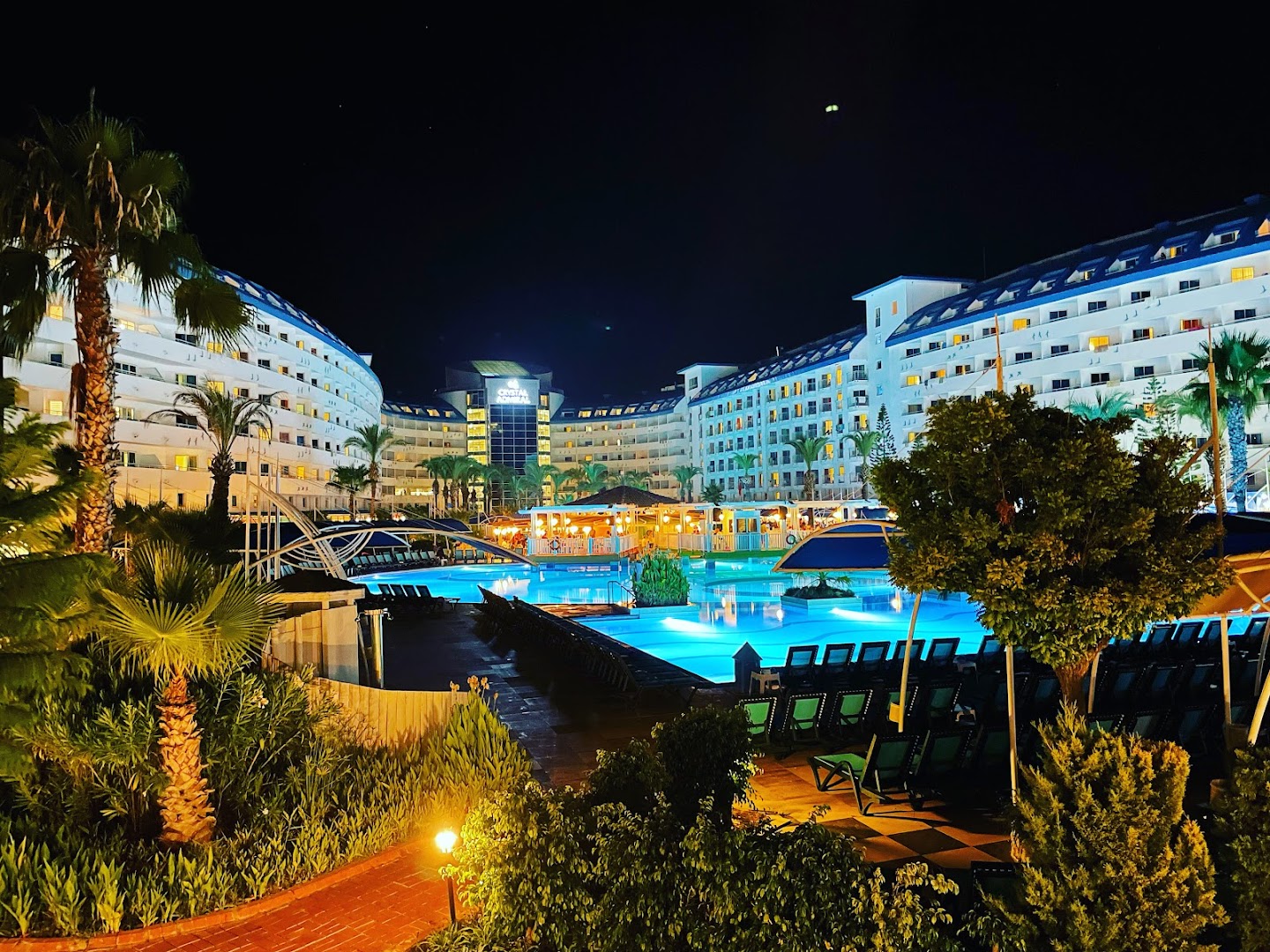 Crystal Admiral Resort Suites & Spa nakts skats uz baseinu — izgaismota viesnīcas arhitektūra un atpūtas krēsli pie ūdens