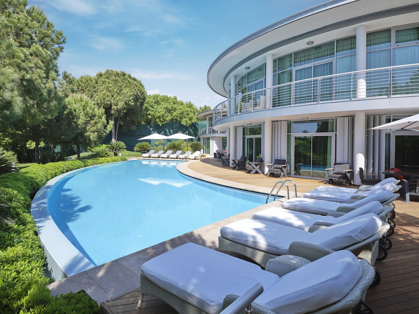 Calista Luxury Resort pusapaļas formas baseins pie viesnīcas korpusa ar baltiem atpūtas krēsliem uz koka terases Belekā