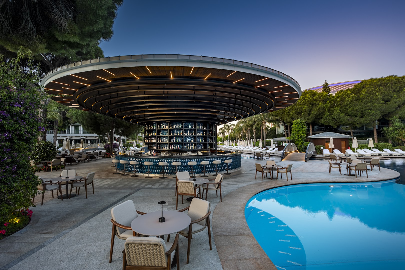 Calista Luxury Resort moderns apaļas formas bārs pie baseina vakarā ar apgaismojumu, galdiņiem un krēsliem Turcijas piekrastē