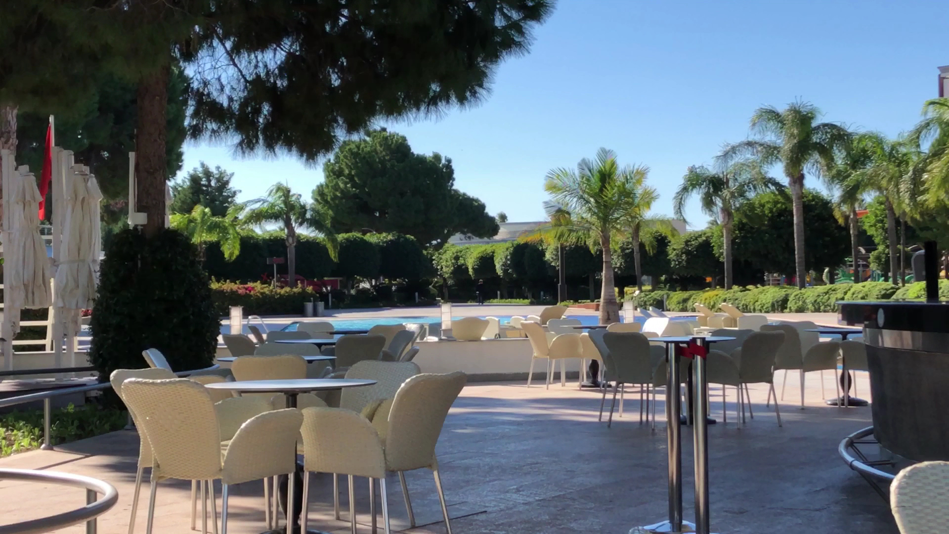 Calista Luxury Resort āra kafejnīca pie baseina ar gaišiem pītiem krēsliem, saulessargiem un zaļojošu dārzu Belekas piekrastē