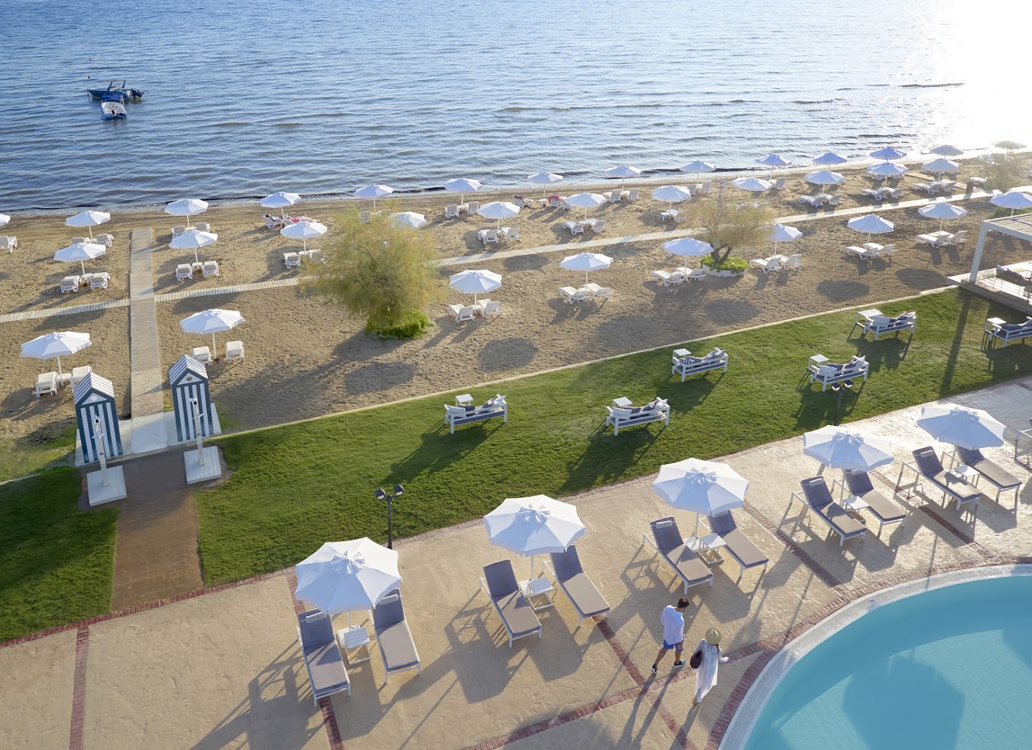 Capo Di Corfu pludmales zona ar saulessargiem un atpūtas krēsliem pie Jonijas jūras Korfu salā — skats no augšas uz zālāju...