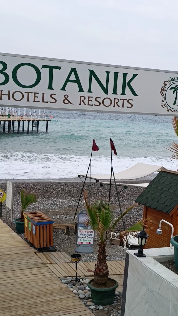 Botanik Platinum pludmales ieeja ar viesnīcas logo, oļu krasts, ūdens sporta aktivitāšu norādes un skats uz jūru