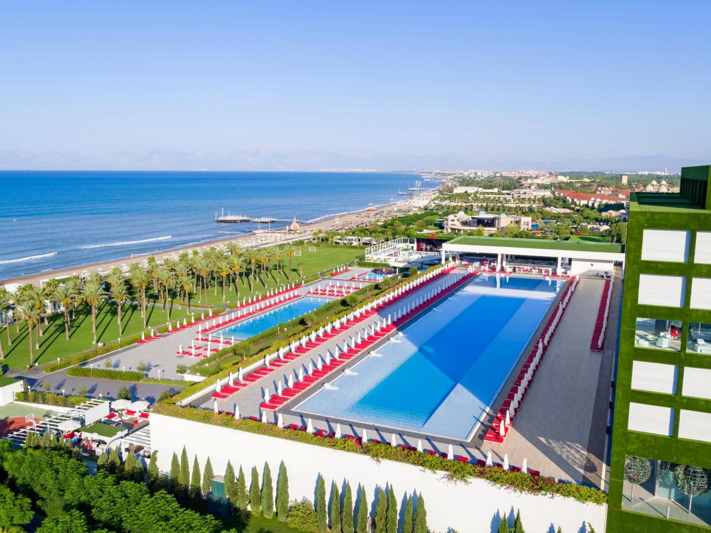 Adam & Eve Hotel panorāmas skats uz galveno baseinu un Vidusjūras piekrasti Belekā — plaša teritorija ar palmām un sauļošanās zonu