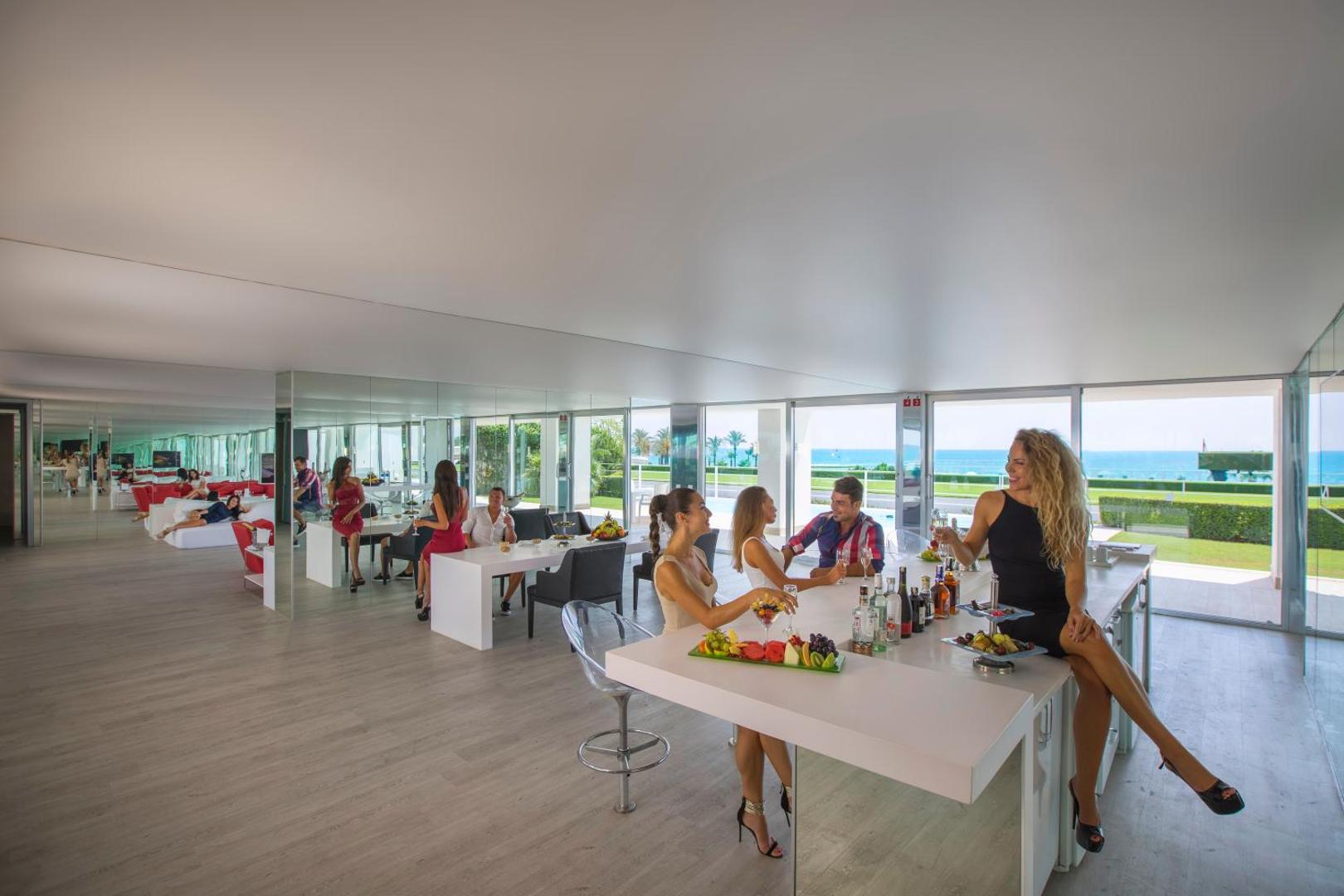 Adam & Eve Hotel modernais bārs un atpūtas telpa ar spoguļiem, kur viesi bauda kokteiļus un skatu uz jūru