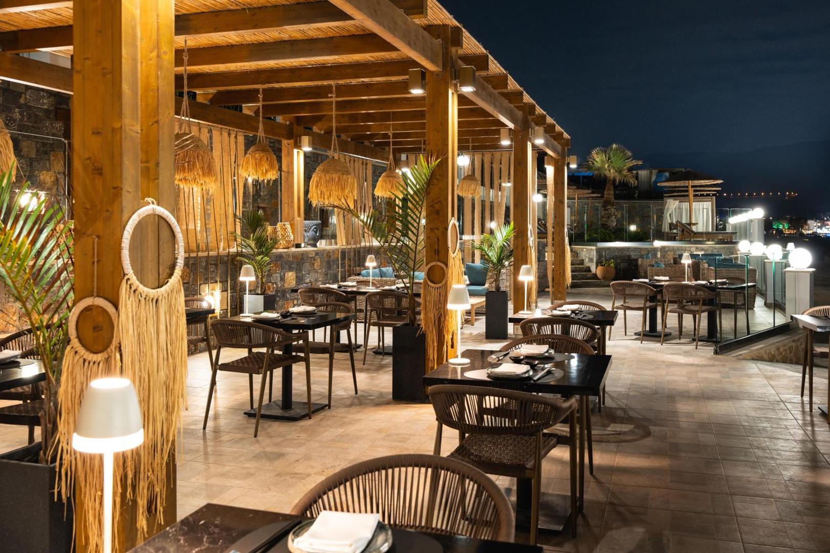 Alexander Beach Hotel & Village modernais āra restorāns vakarā ar stilīgu apgaismojumu, koka pergolu un dizaina mēbelēm