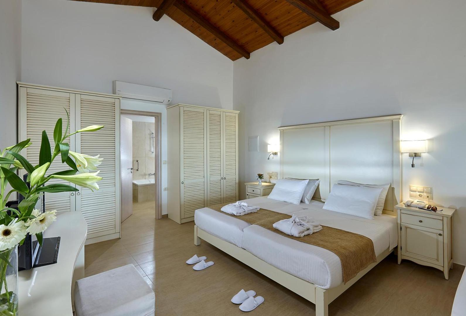 Alexander Beach Hotel & Village numurs ar augstiem koka griestiem, gaišām mēbelēm un skatu uz vannasistabu