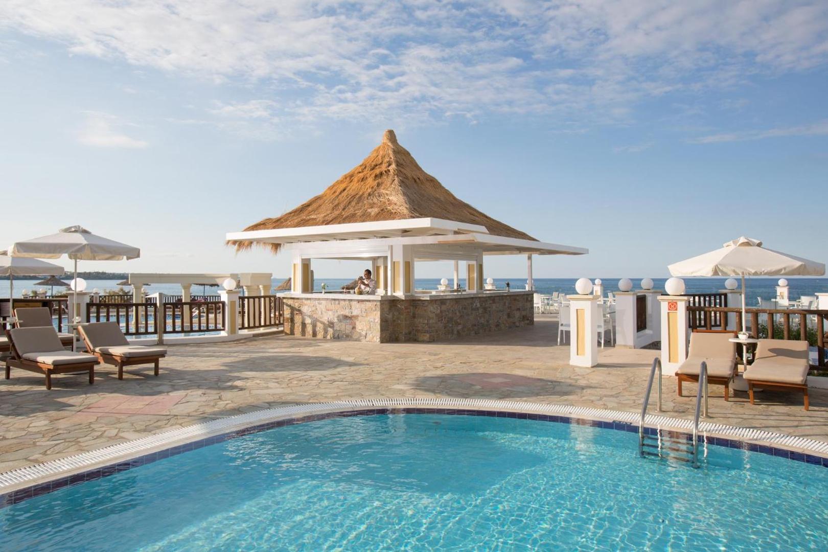 Alexander Beach Hotel & Village baseina bārs ar salmu jumtu un atpūtas zonu saulainā dienā Malijā, Krētā