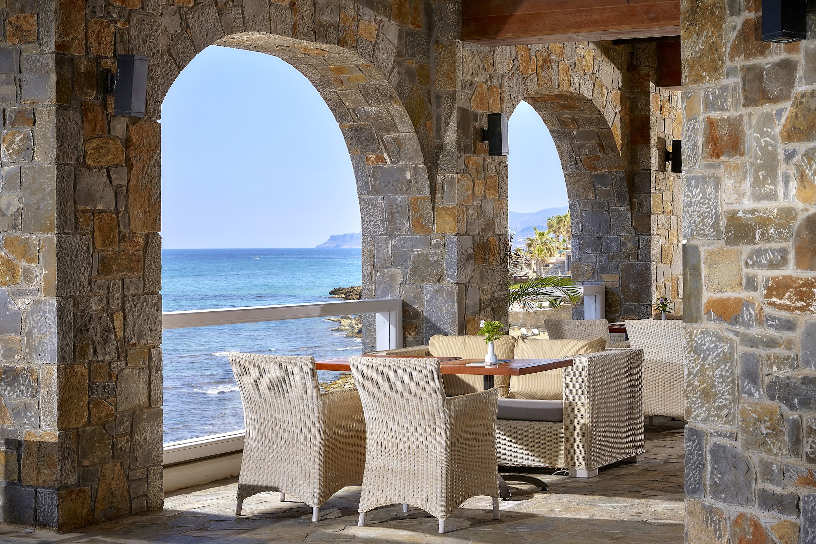 Alexander Beach Hotel & Village restorāna terase ar akmens arkām un pītiem krēsliem, no kuras paveras skats uz jūru