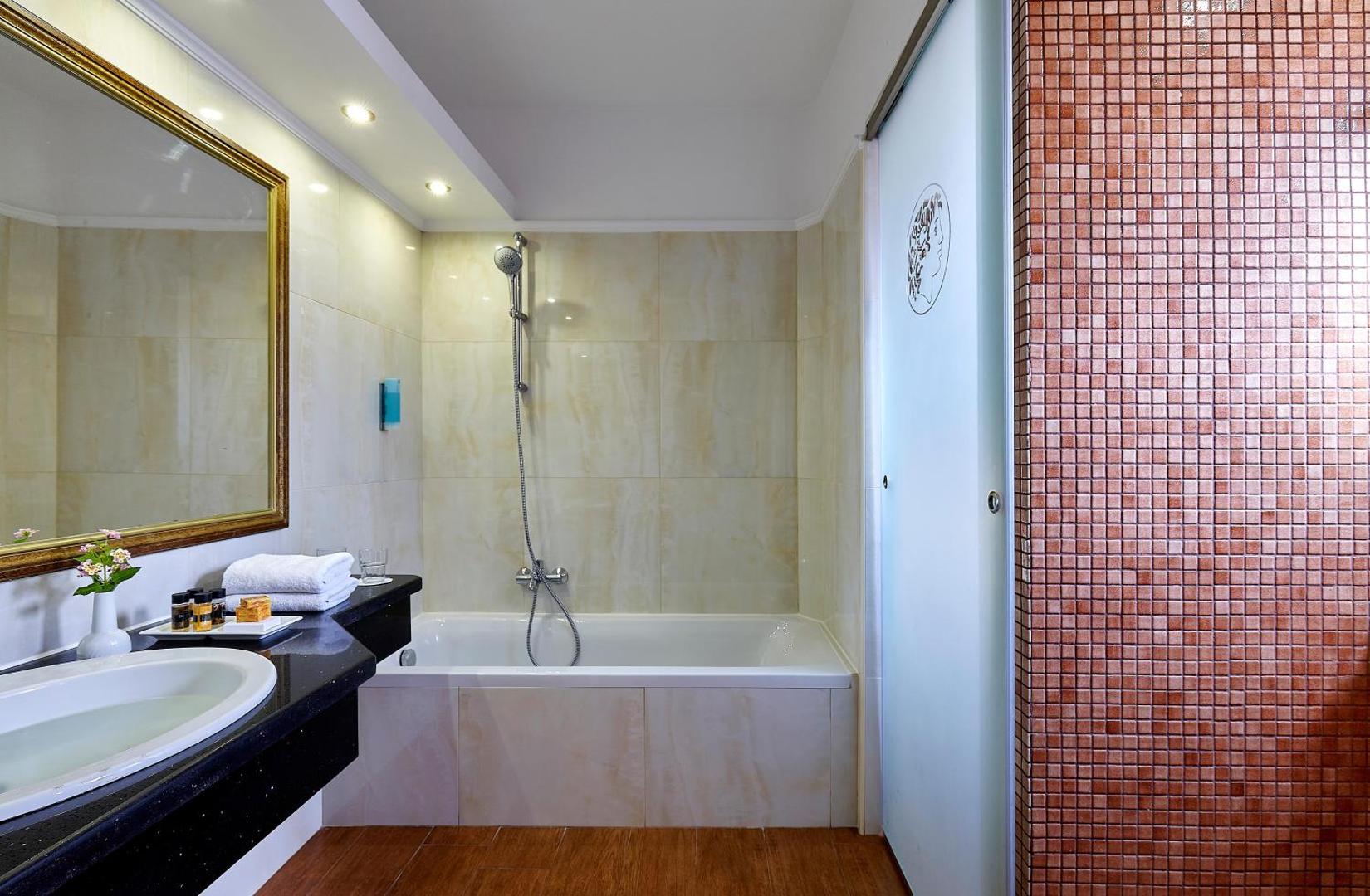 Alexander Beach Hotel & Village numura vannas istaba ar melnu virsmu, vannu un mozaīkas flīžu sienu Krētā