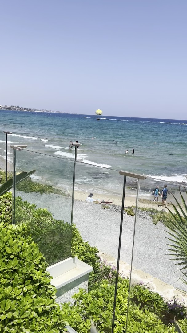 Skats no Alexander Beach Hotel & Village terases uz Vidusjūru Malijā, Krētā — redzama pludmale, atpūtnieki un paraseilings tālumā