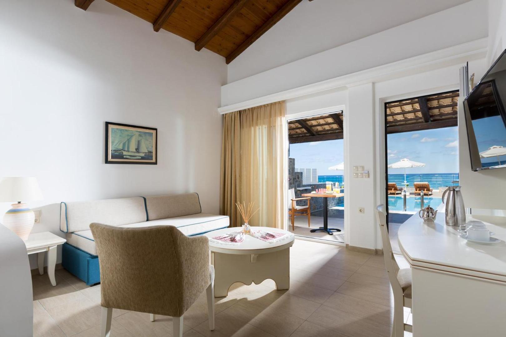 Alexander Beach Hotel & Village viesistabas zona ar dīvānu un terasi, kas ved tieši pie koplietošanas baseina