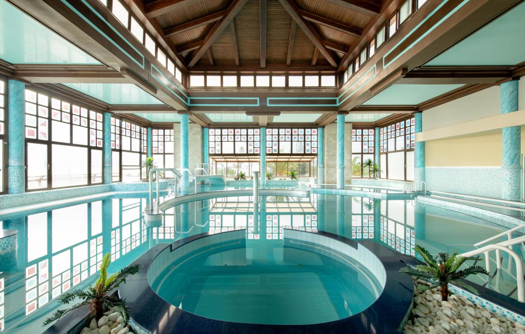 Mitsis Royal Mare iekštelpu baseins un spa centrs ar koka griestu konstrukcijām, panorāmas logiem un džakuzi zonu
