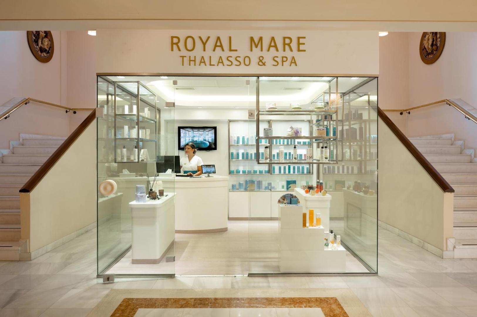 Mitsis Royal Mare Thalasso & Spa centra recepcija un kosmētikas veikals ar stikla vitrīnām un gaišu interjeru
