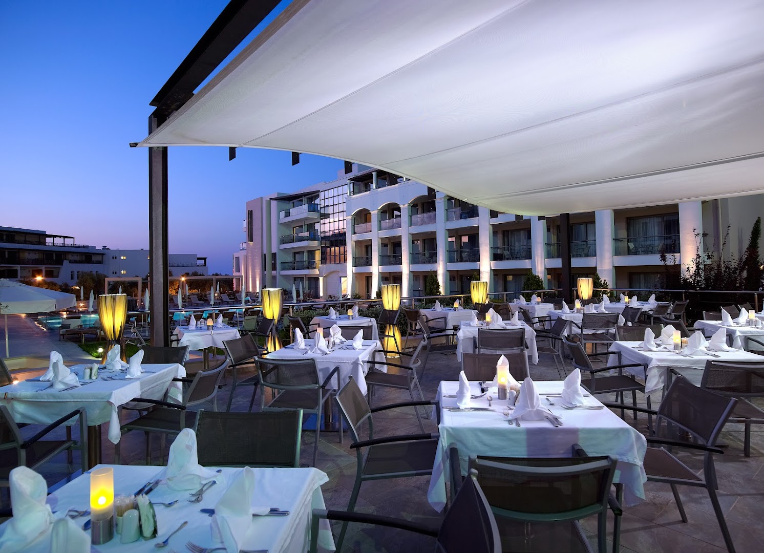 Albatros Spa & Resort āra restorāna terase vakarā ar klātiem galdiem, romantisku apgaismojumu un skatu uz viesnīcas korpusiem Krētā.