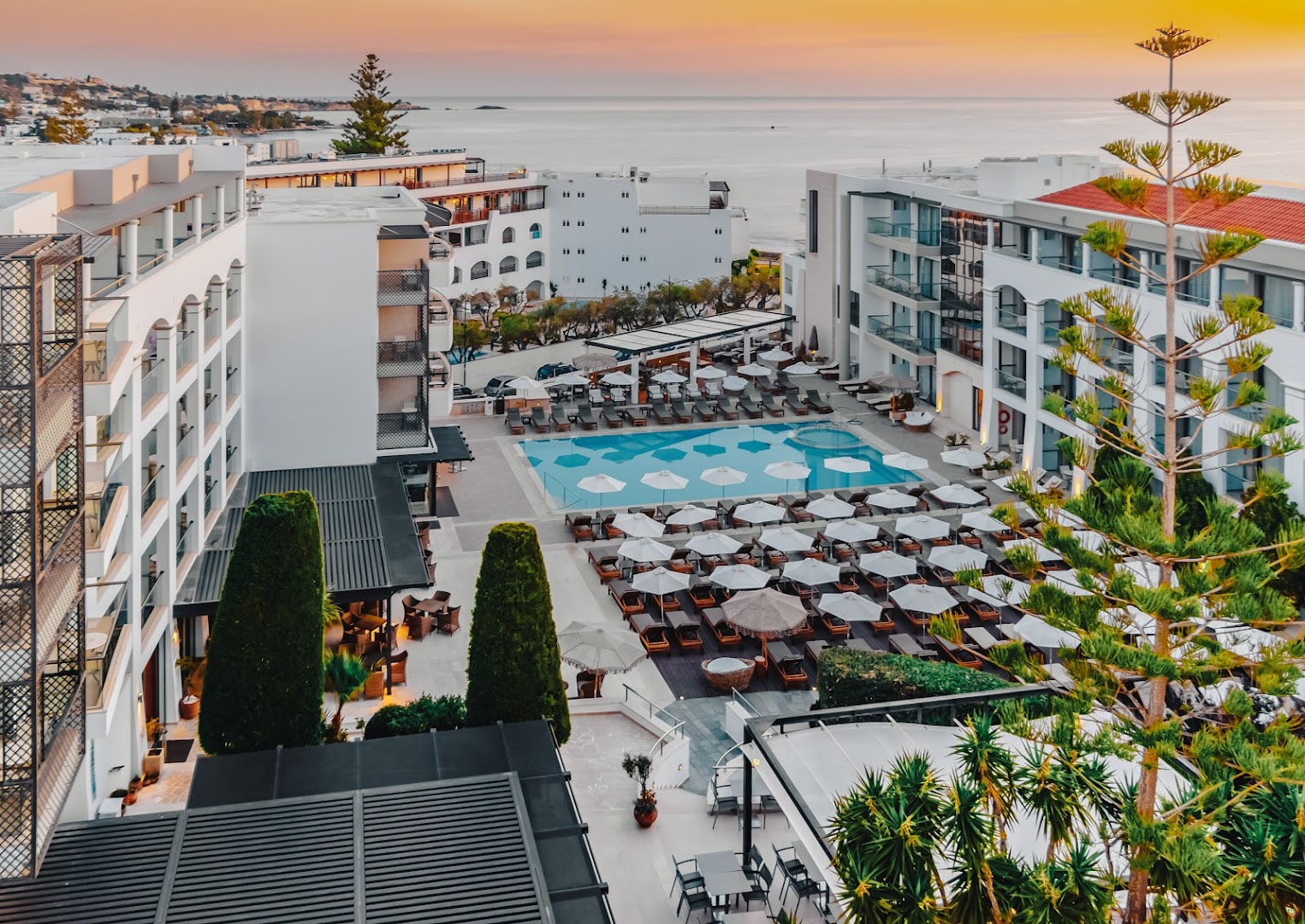Albatros Spa & Resort viesnīcas pagalms ar baseinu, saulessargiem un skatu uz jūru saulrietā Hersonisā, Krētā.