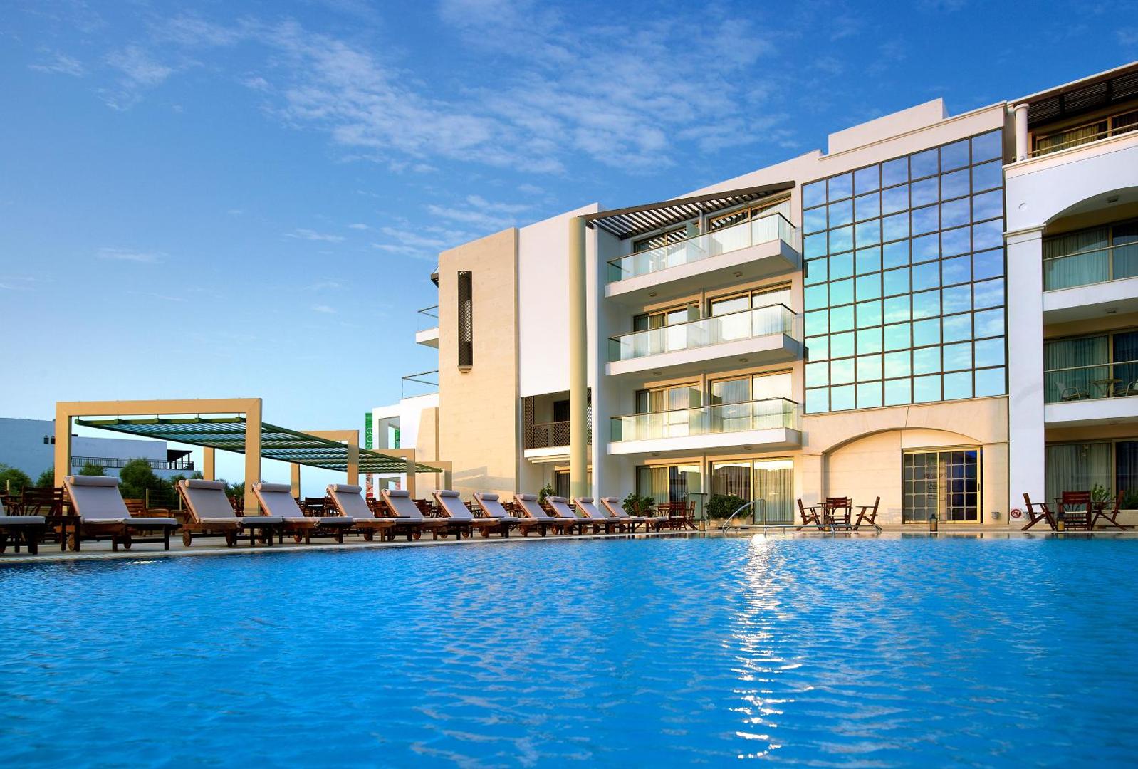 Albatros Spa & Resort viesnīcas fasāde un lielais āra baseins ar sauļošanās krēsliem Hersonisas kūrortā, Krētā