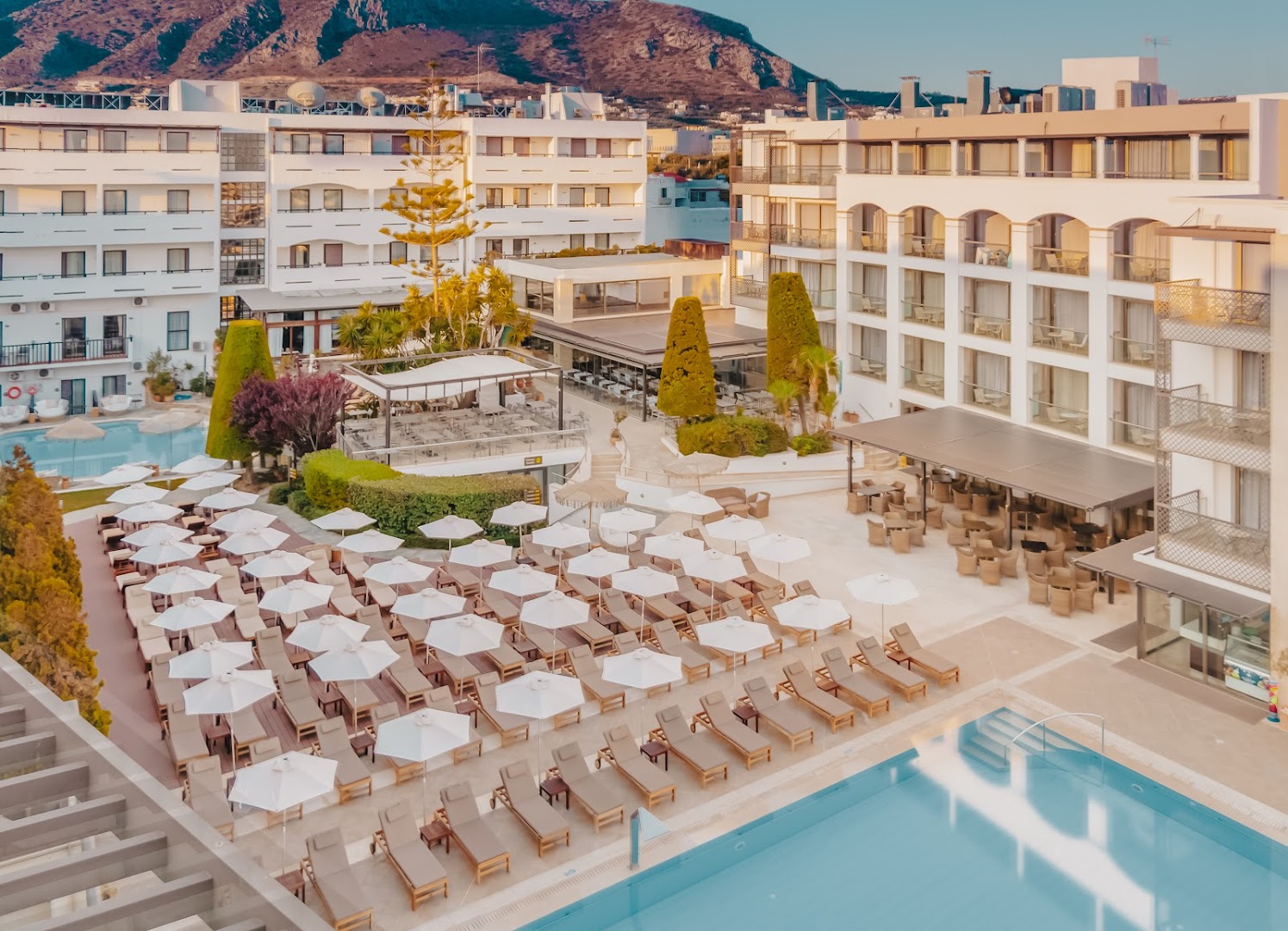 Albatros Spa & Resort atpūtas zona ar daudziem sauļošanās krēsliem, saulessargiem un baseinu uz kalnu fona.