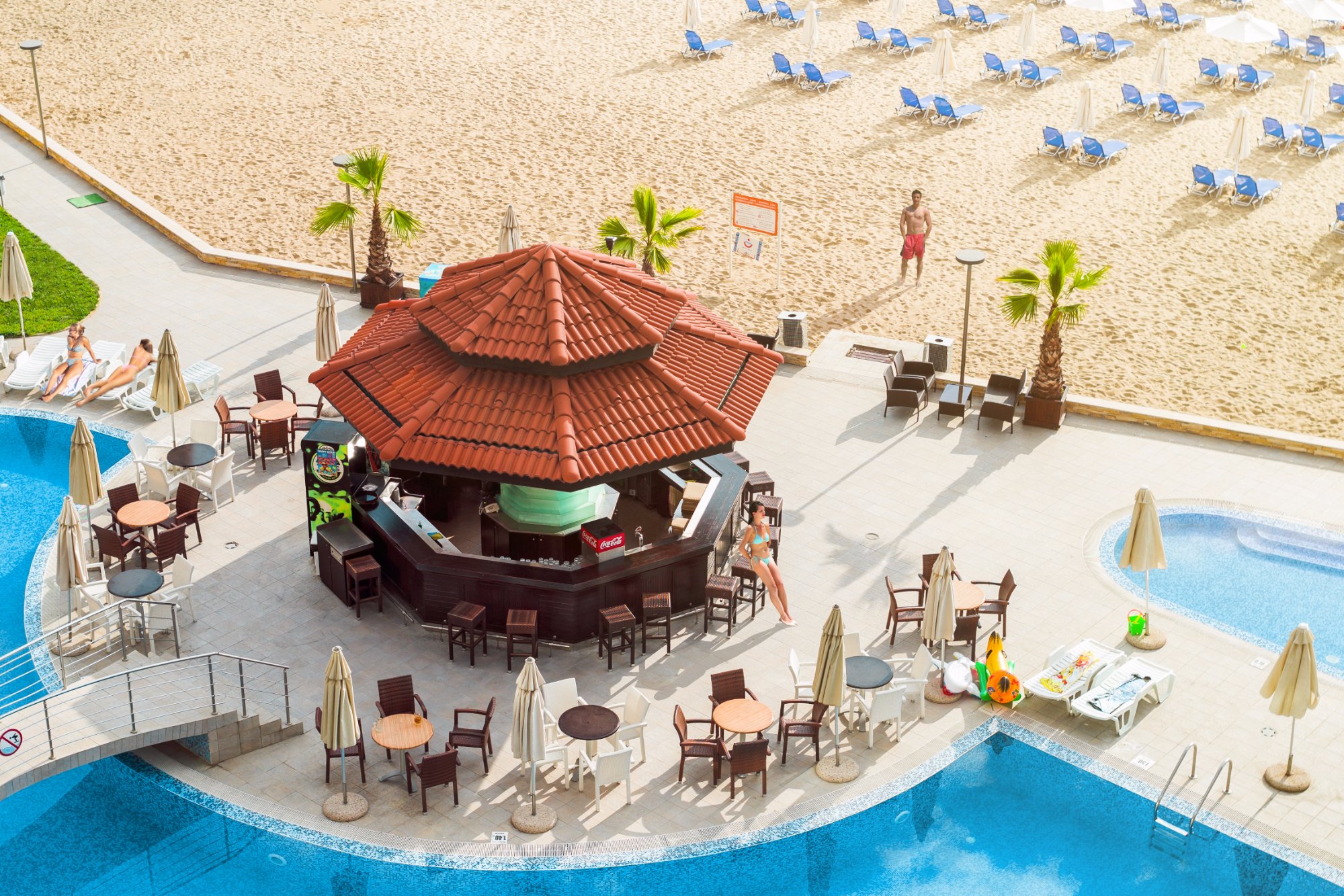 Obzor Beach Resort bārs pie baseina ar koka apdari un galdiņiem, fonā plaša smilšu pludmale un jūra Bulgārijas piekrastē