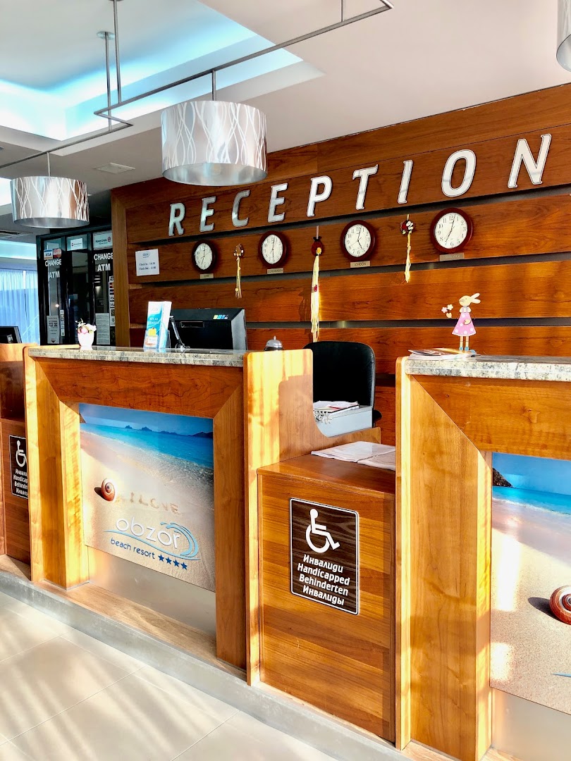 Obzor Beach Resort viesnīcas recepcija ar koka apdari, pulksteņiem un informāciju par pieejamību cilvēkiem ar kustību traucējumiem