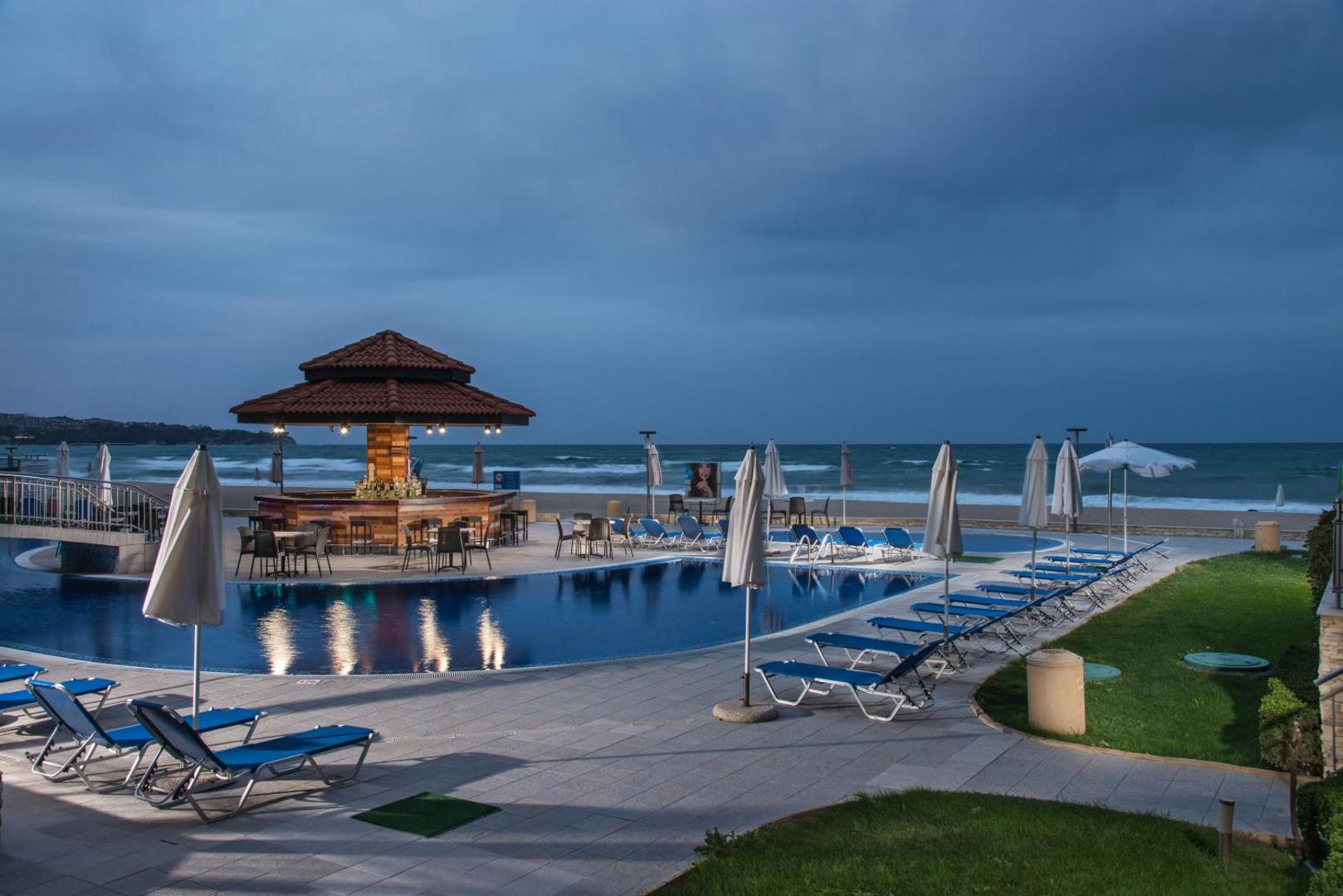 Obzor Beach Resort baseins un bārs krēslas stundā pie Melnās jūras krasta Obzorā — sauļošanās krēsli un mierīga atmosfēra
