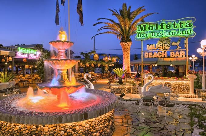 Molfetta Beach Hotel āra terase vakarā ar izgaismotu strūklaku un bāru pie jūras — Molfetta Bar Restaurant Korfu